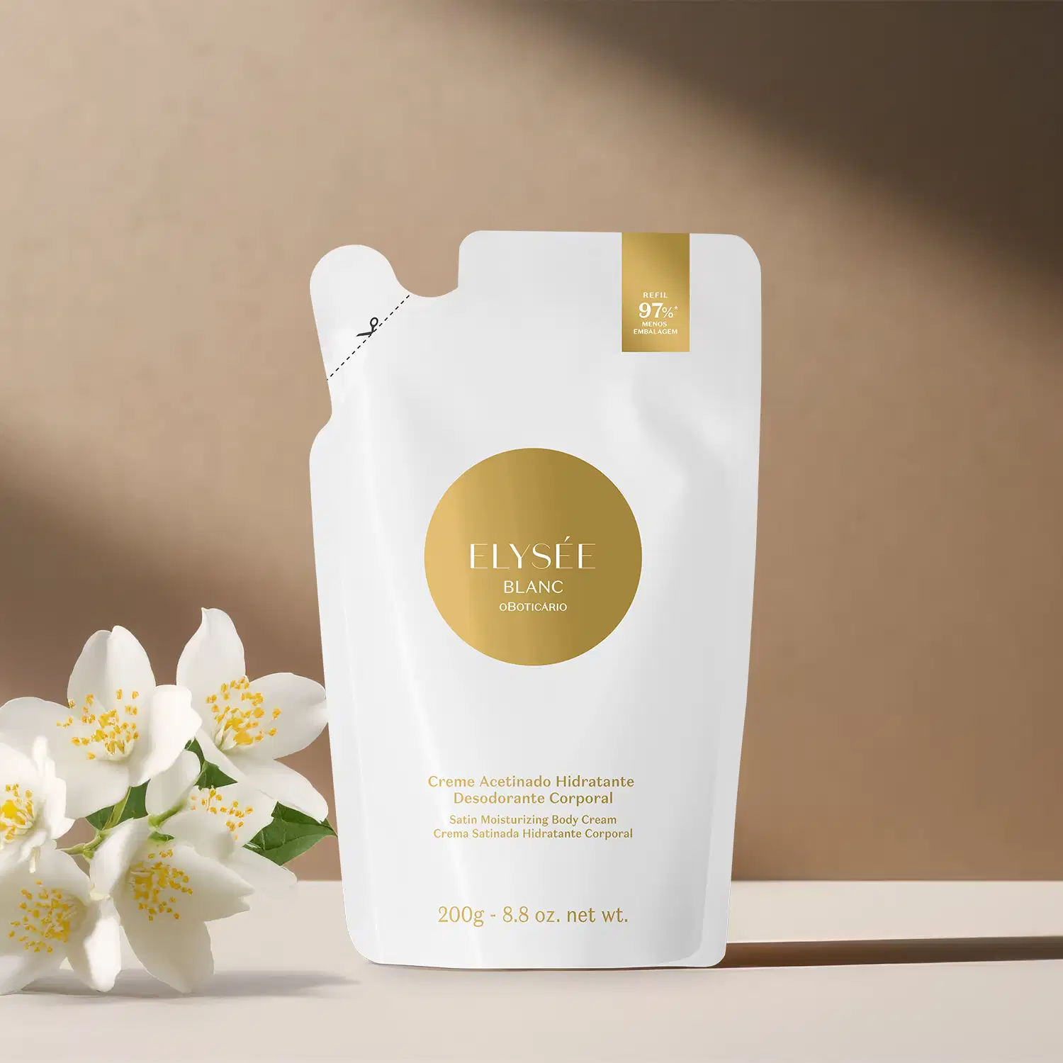 Refil de creme hidratante corporal acetinado da marca Elysée Blanc em sachê nas cores branca e dourada. posicionado sobre superfície bege ao lado de flores brancas com sombra natural ao fundo.