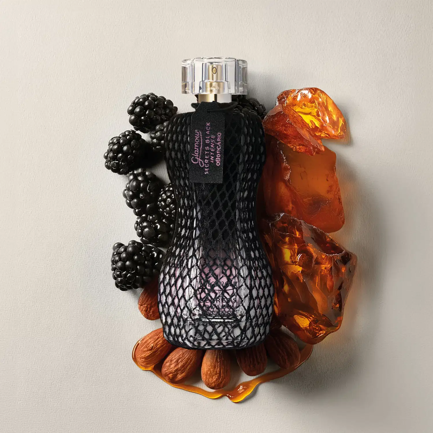 Frasco de desodorante colônia Glamour Secrets Black Intense em ambiente com amoras e âmbar, sobre superfície clara.