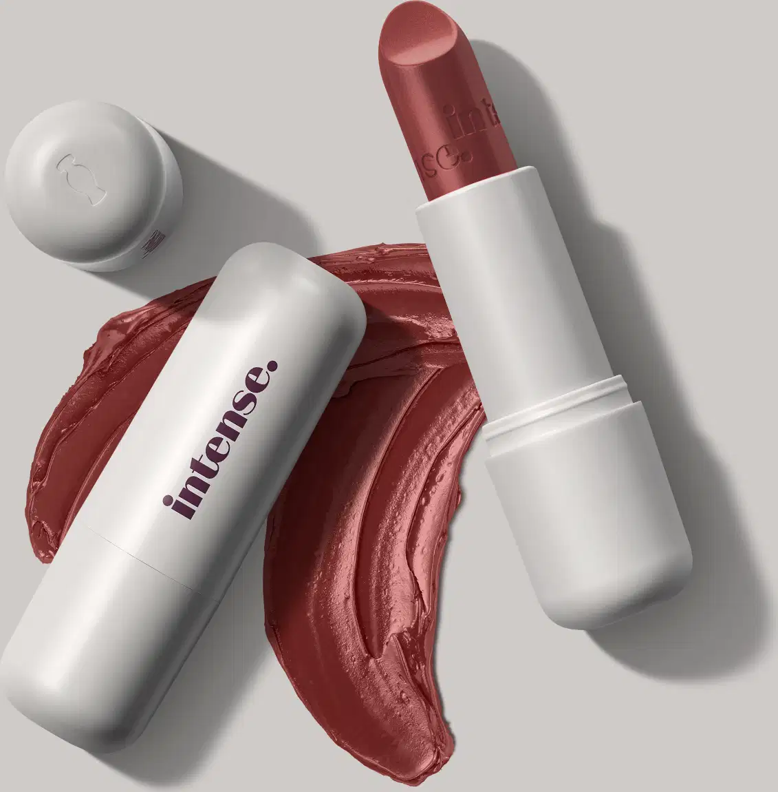 Batom cremoso na cor rosa 227 da marca Intense, em embalagem toda branca com letras pretas na tampa, com uma quantidade de produto espalhada no fundo cinza.