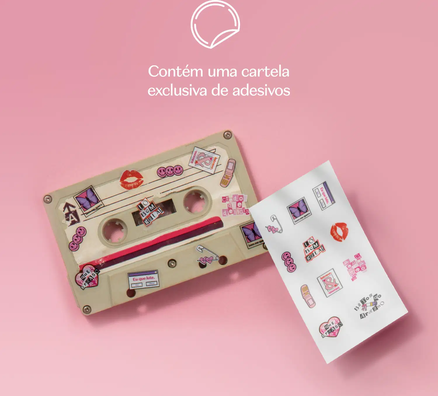 Fita K7 em tons de bege com vários adesivos, ao lado de uma cartea de adesivos em fundo rosa.