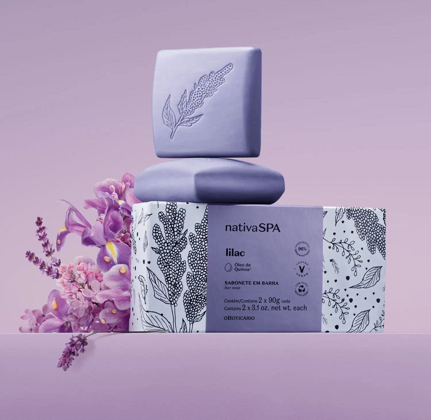 Caixa branca com faixa lilás e ilustrações na cor preta ao lado de dois sabonetes em barra quadrados na cor lilás da marca Nativa SPA Lilac em um cenário com flores lilás ao redor e fundo na mesma tonalidade.