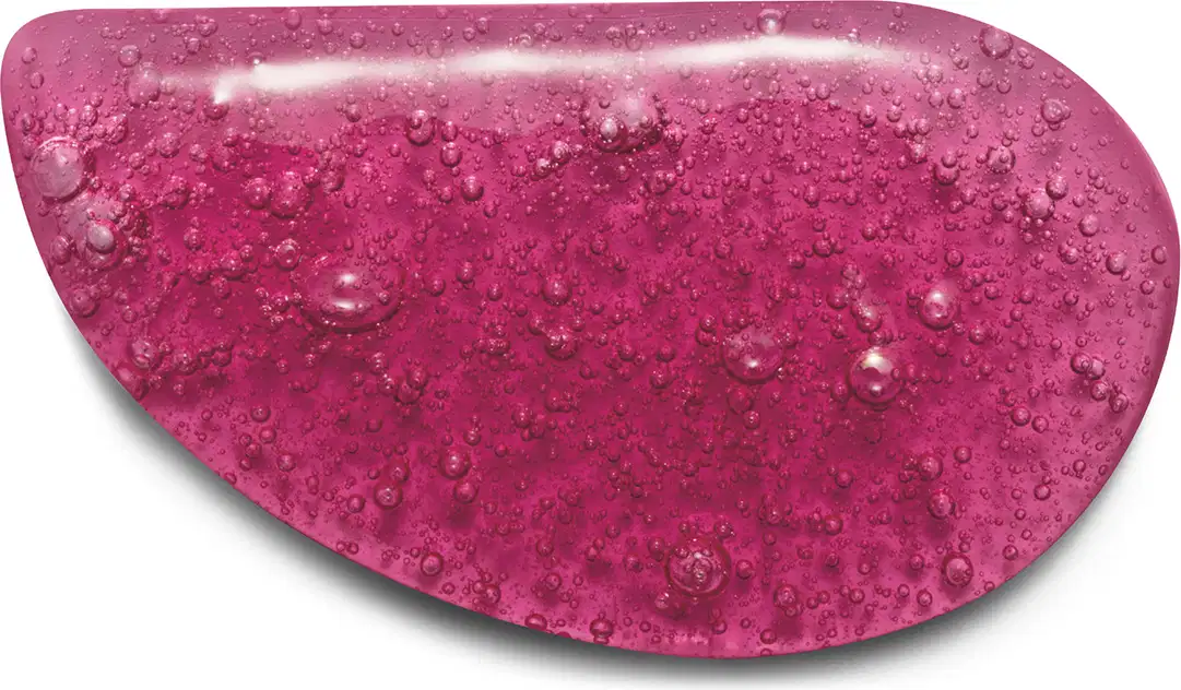 Textura do sabonete vegetal em formato oval irregular, com uma cor rosa vibrante e brilhante. A superfície apresenta pequenas bolhas e gotas de água, dando um aspecto molhado e texturizado. Não há rótulos ou texto visível.