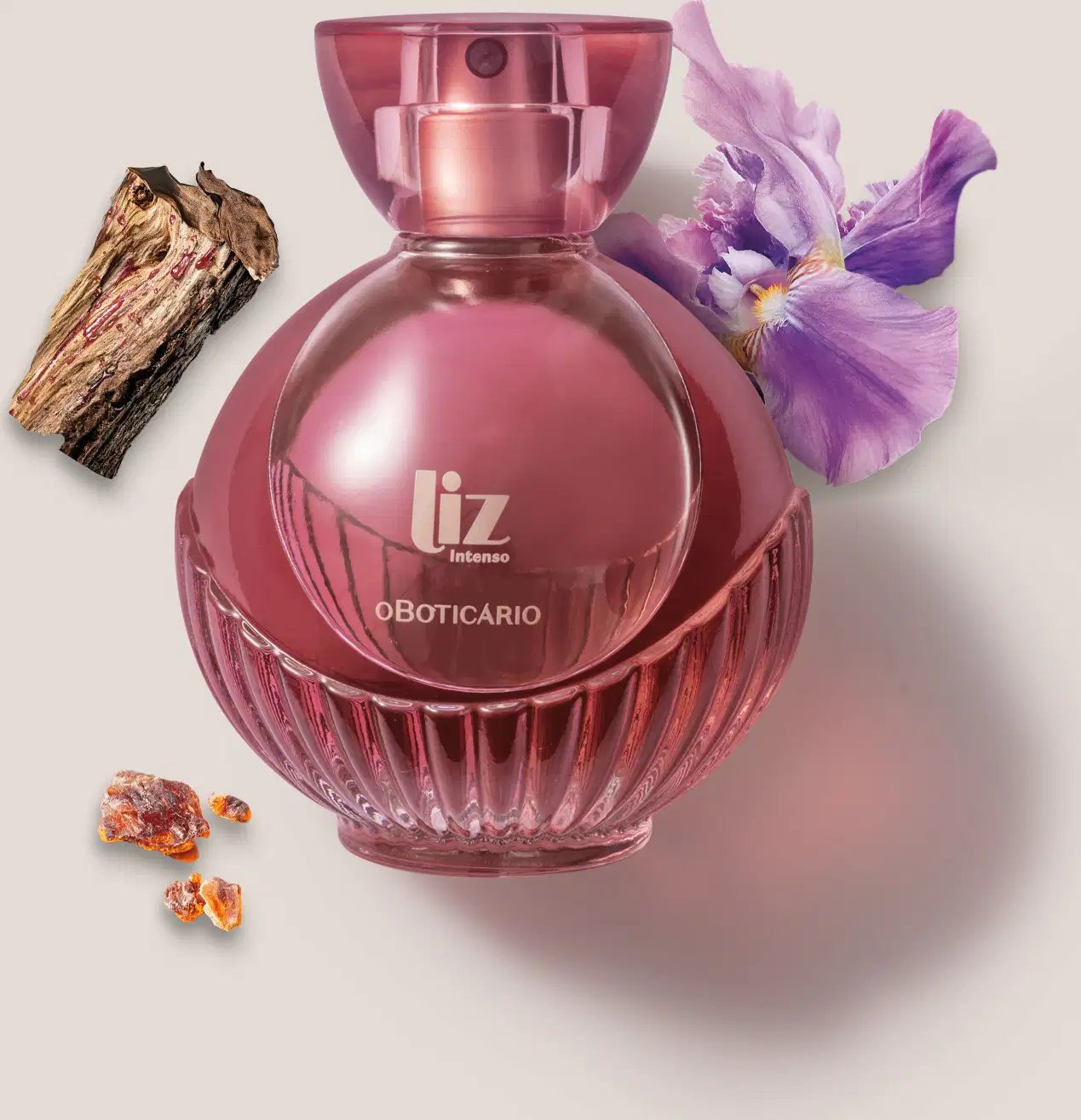 Um vidro com líquido vermelho, borrifador dourado, tampa transparente e letras douradas de desodorante colônia Liz Intenso está em um fundo cinza com flor roxa, pedaço de madeira e âmbar ao redor.
