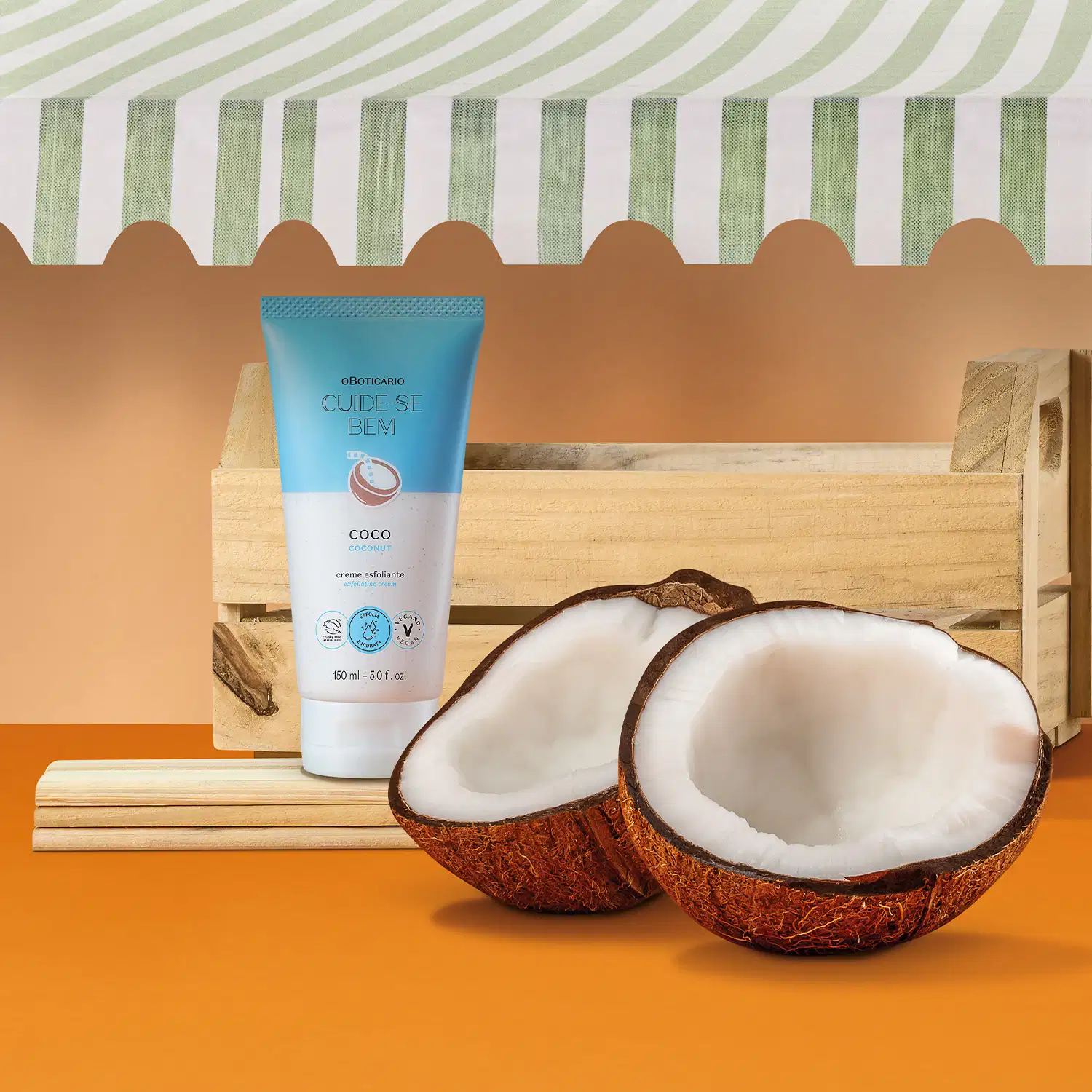 Bisnaga azul e branca com coco ilustrado contendo creme esfoliante corporal Cuide-se Bem Feira Coco em caixa de madeira, com coco cortado ao lado, sobre fundo laranja e listras verdes e brancas.