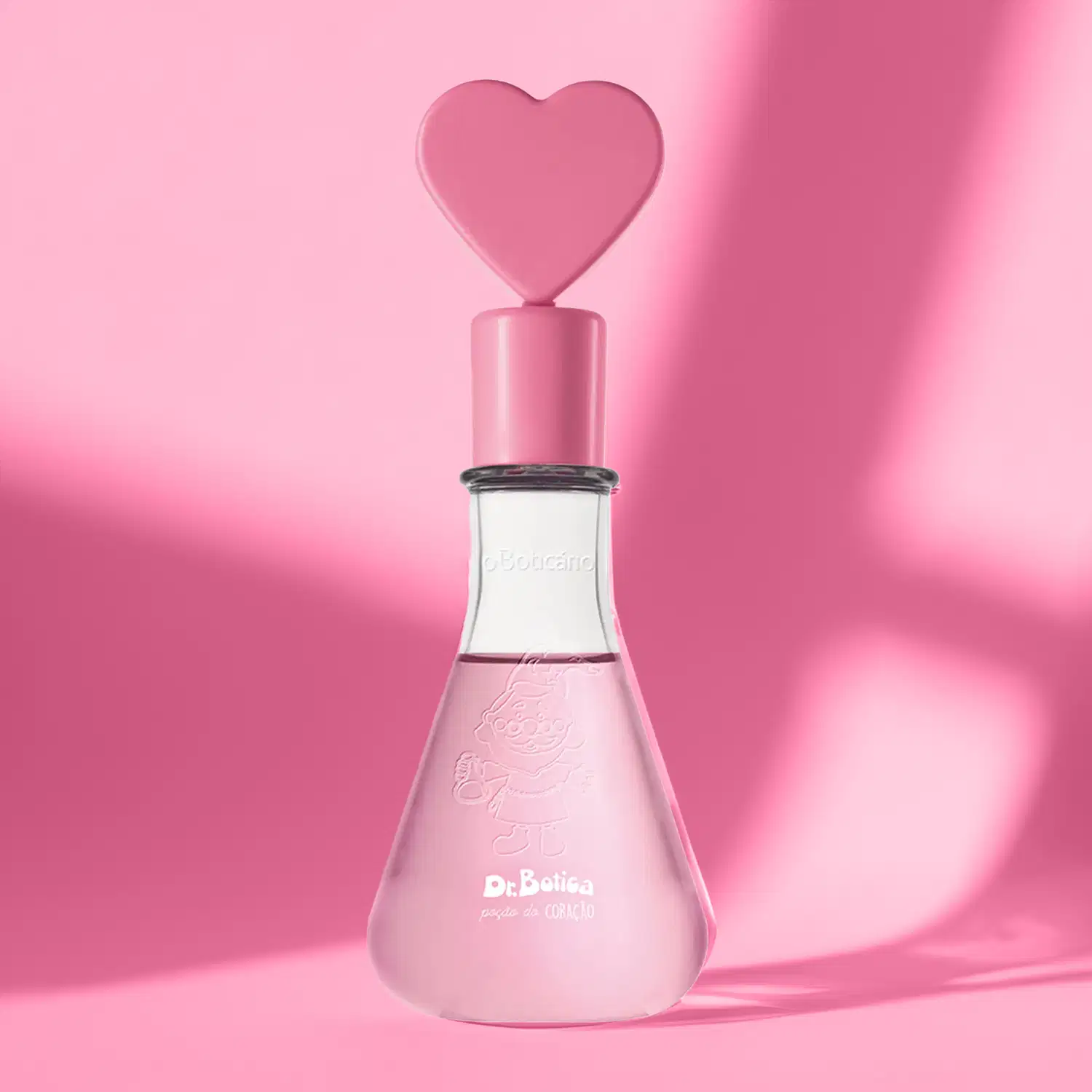 Frasco transparente em formato de vidro laboratorial com líquido rosa, tampa também rosa com coração na ponta e letras brancas no rótulo de colônia infantil Dr. Botica Poção do Coração em fundo rosa com sombras.