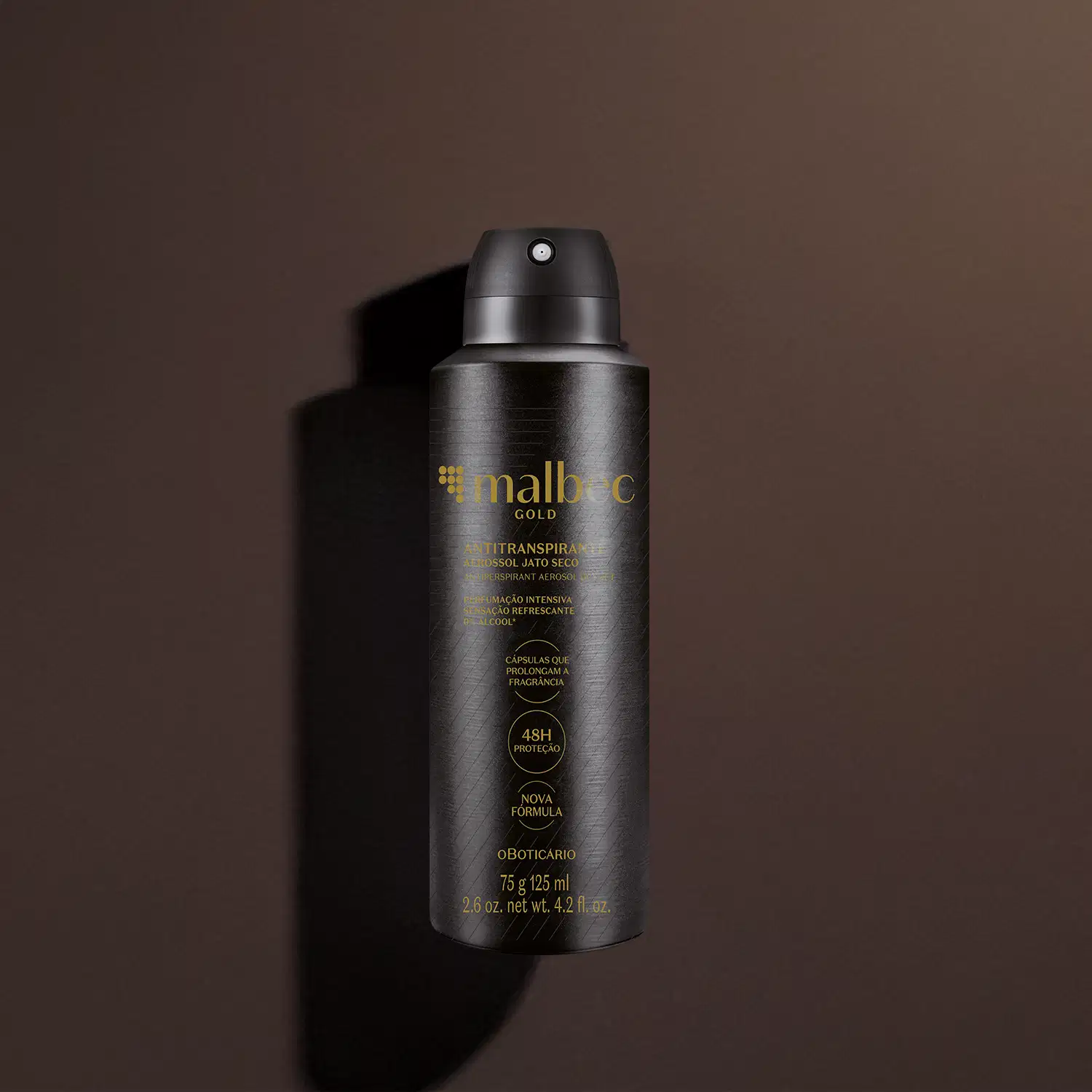 Imagem de um frasco preto de desodorante antitranspirante aerossol da marca Malbec Gold, com rótulo em dourado. Ele está em um fundo cinza escuro e há uma sombra, compondo um cenário forte e elegante.