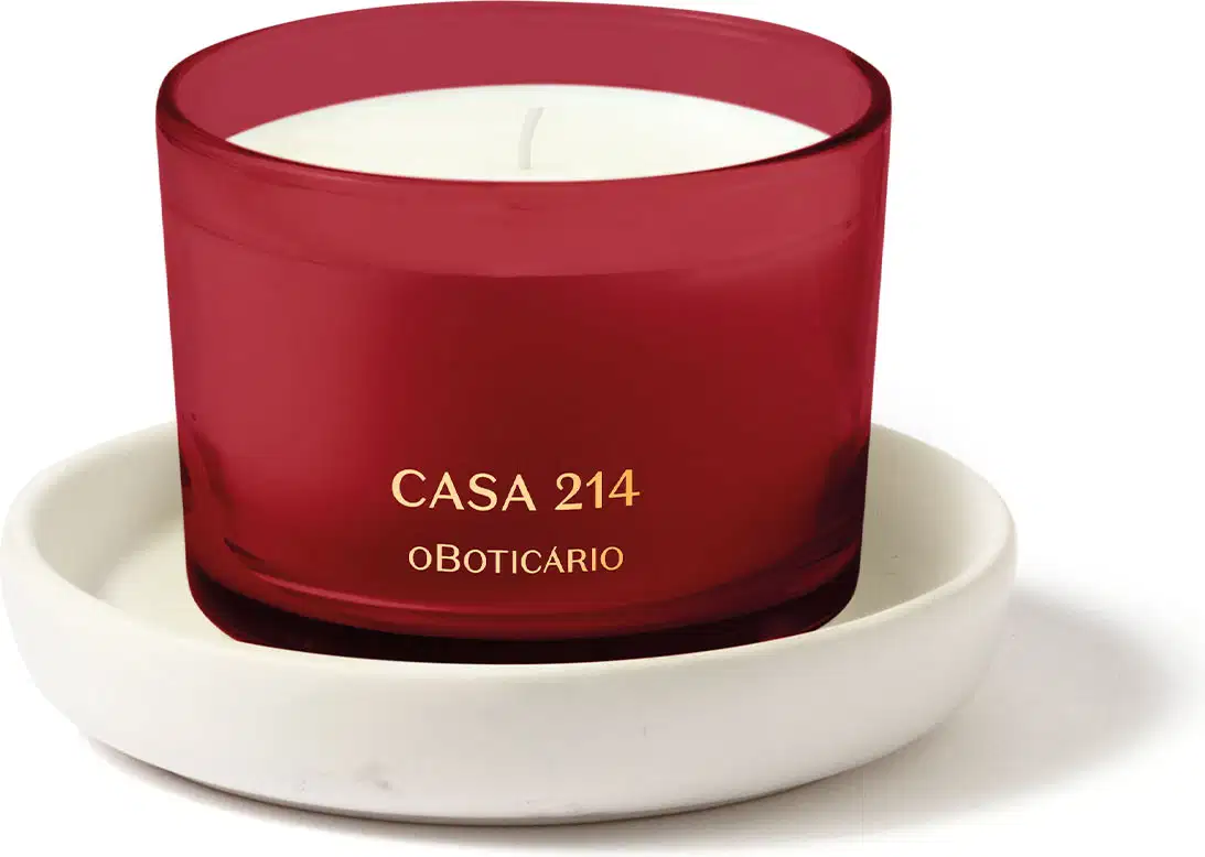 Vela perfumada branca em recipiente vermelho acompanhada de um suporte para velas branco, ambos da marca Casa 214.