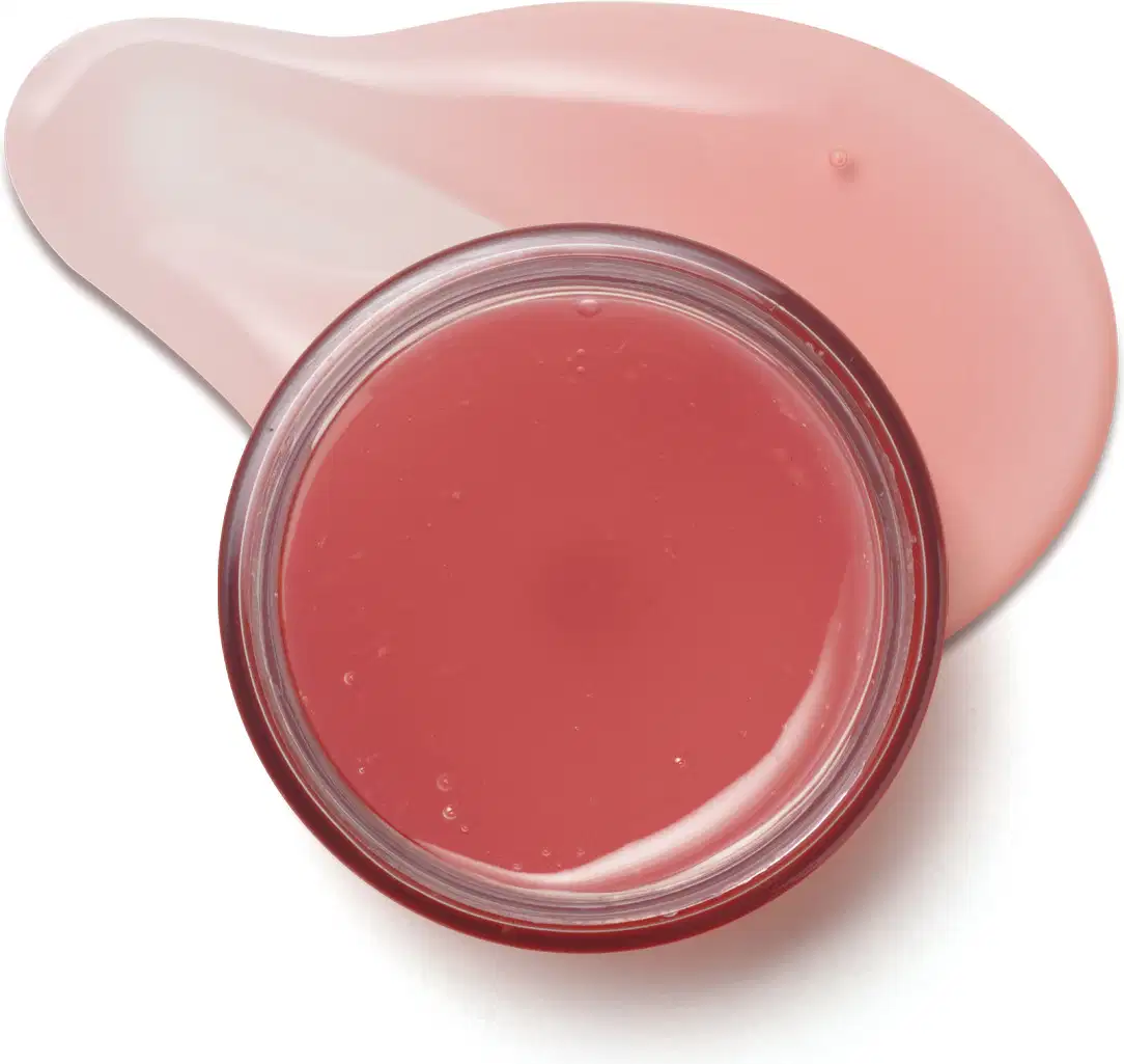 Pote redondo aberto contendo máscara facial noturna Cuide-se Bem Feira Melancia e um pouco do creme em gel vermelho espalhado na superfície branca.