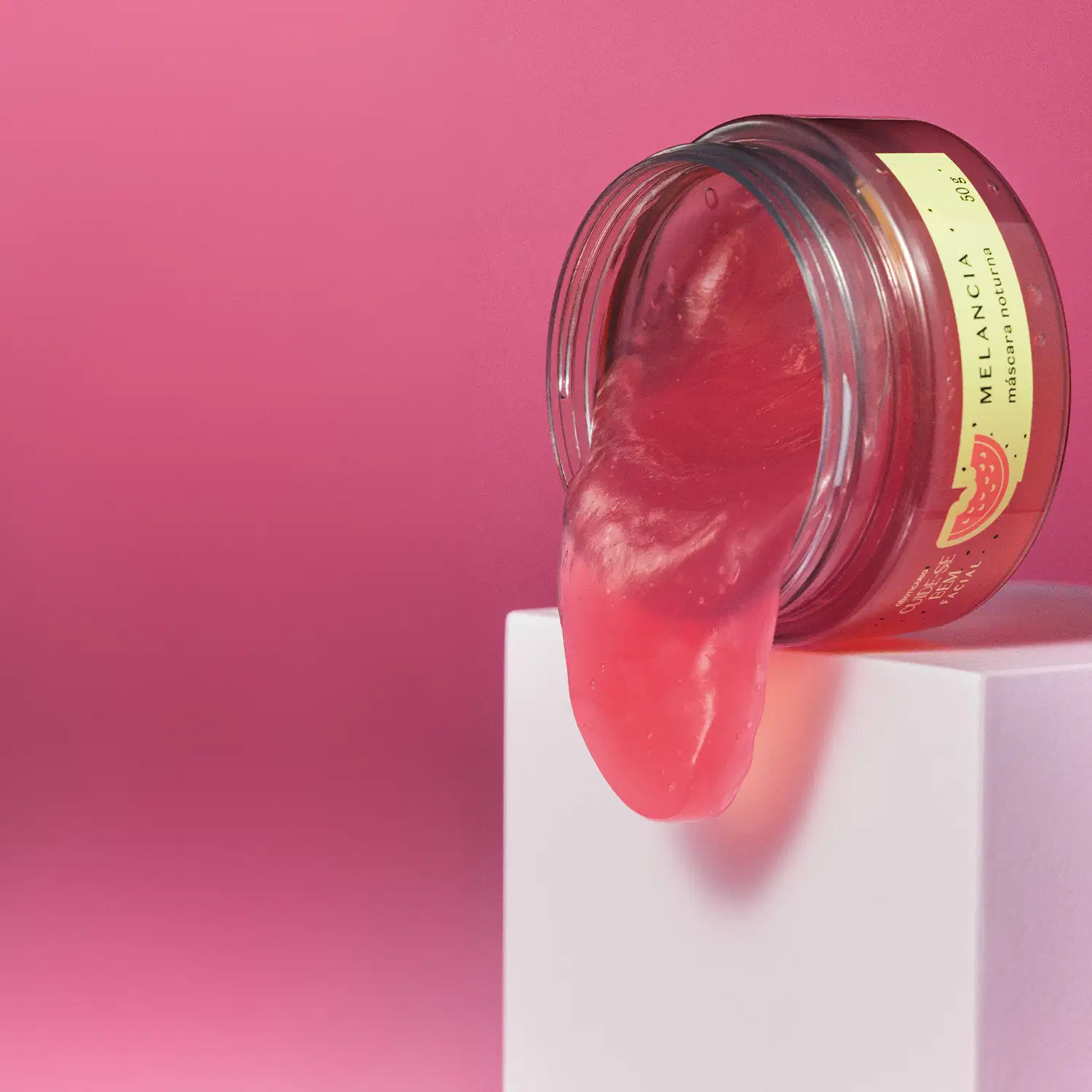 Pote com creme vermelho, tampa verde e rótulo também verde com melancia ilustrada contendo máscara facial noturna Cuide-se Bem Feira Melancia virado, derramando um pouco do creme em gel vermelho na superfície branca com fundo vermelho.