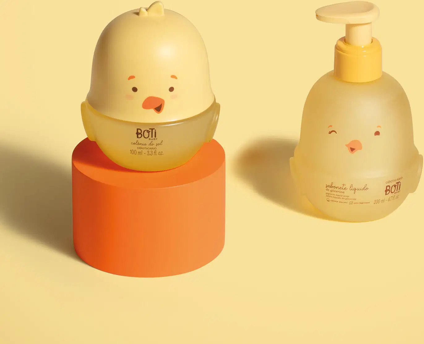 Dois frascos em forma de pintinhos amarelos com detalhes em laranja, sendo um de colônia do sol e outro, com bomba dosadora laranja, de sabonete líquido de glicerina. Os produtos estão em fundo laranja.