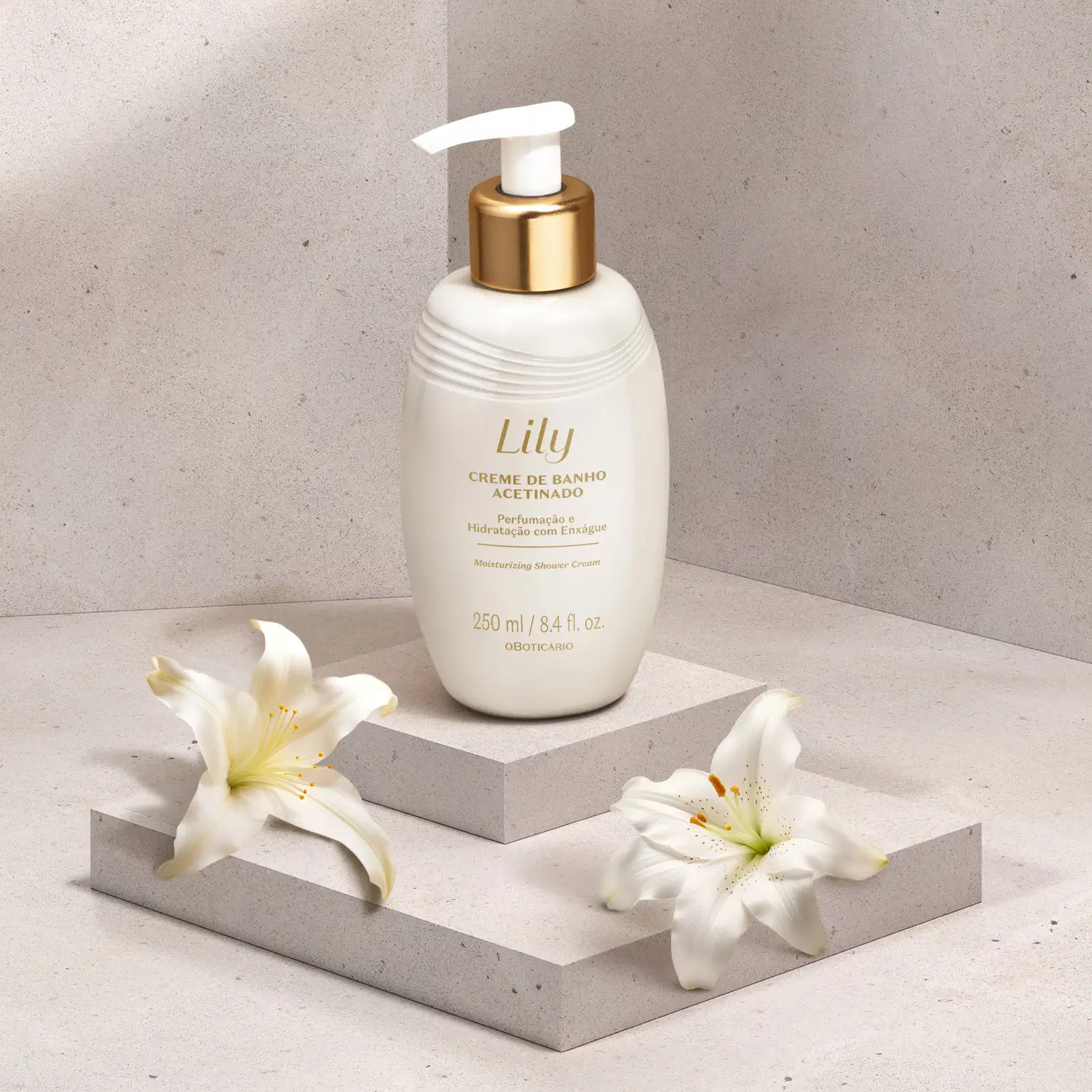 Frasco branco ovalado com detalhe dourado, tampa dosadora branca e letras bege escuras de creme de banho acetinado da marca Lily em plataforma branca com flores brancas ao redor e fundo cinza.
