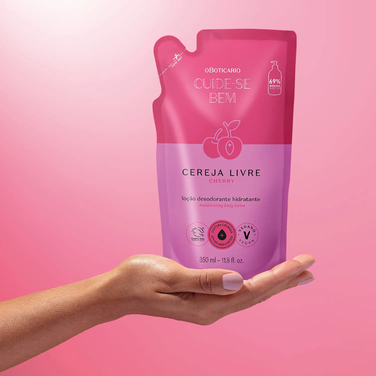 Mão segurando um refil de loção hidratante corporal Cuide-se Bem Cereja Livre em sachê nas cores rosa e roxo com cerejas ilustradas. A imagem está em fundo em tons de rosa.