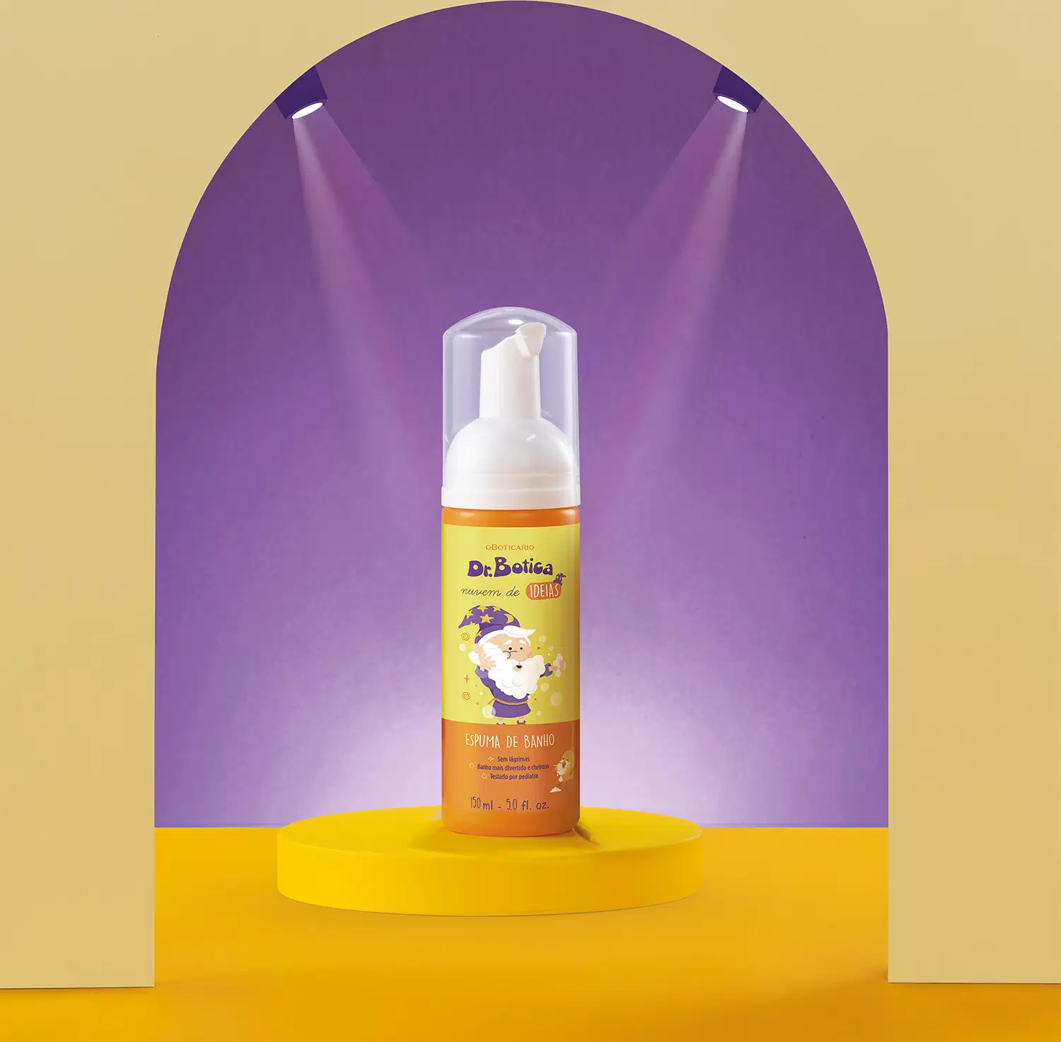Espuma de banho corporal Nuvem de Ideias Dr. Botica em frasco com tampa branca e rótulo amarelo e laranja com ilustração do personagem da marca em destaque sobre superfície amarela, com iluminação roxa ao fundo, criando um ambiente vibrante e atraente.