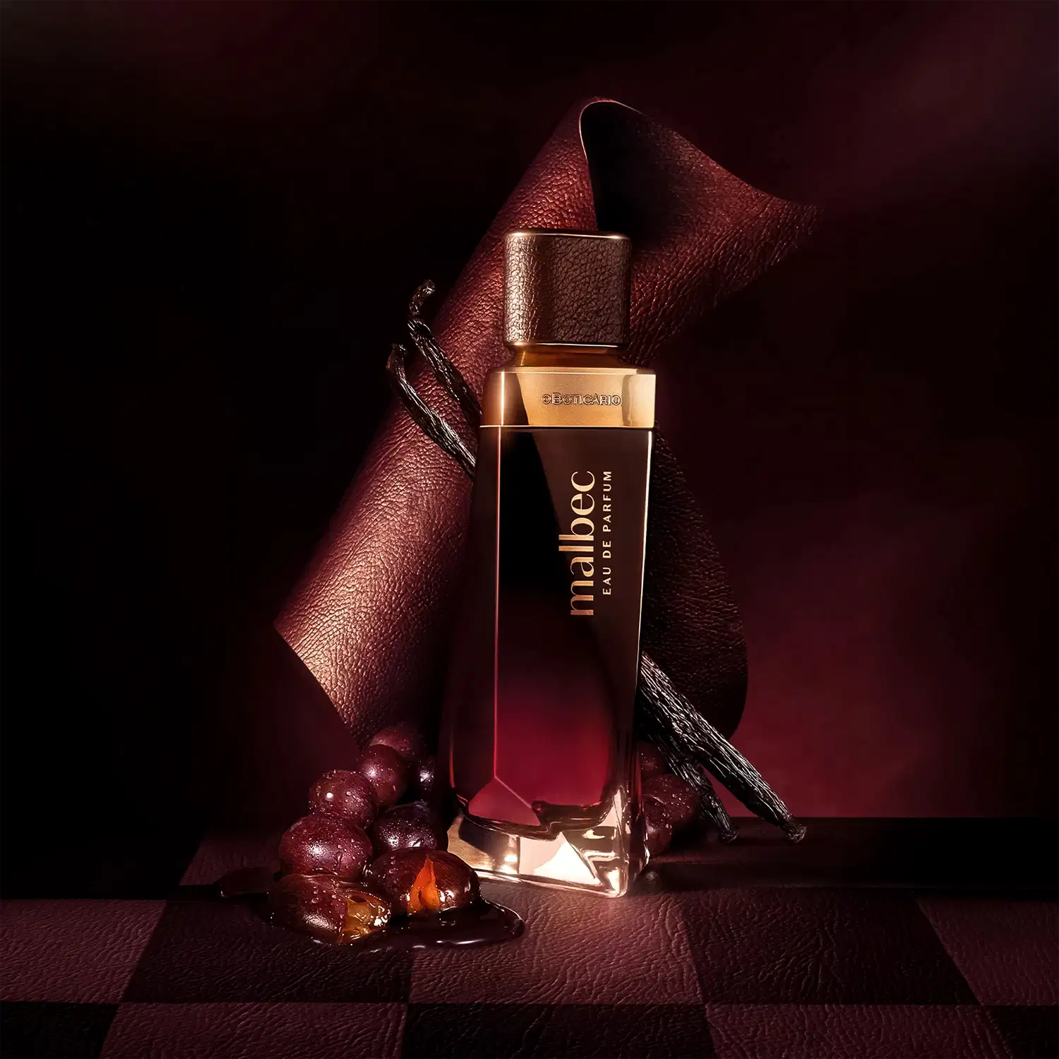Ambiente escuro e elegante, com tons de vermelho e marrom, destacando um frasco de perfume da marca Malbec, acompanhado de uvas e outros elementos decorativos, sugerindo uma ocasião sofisticada de uso do produto.