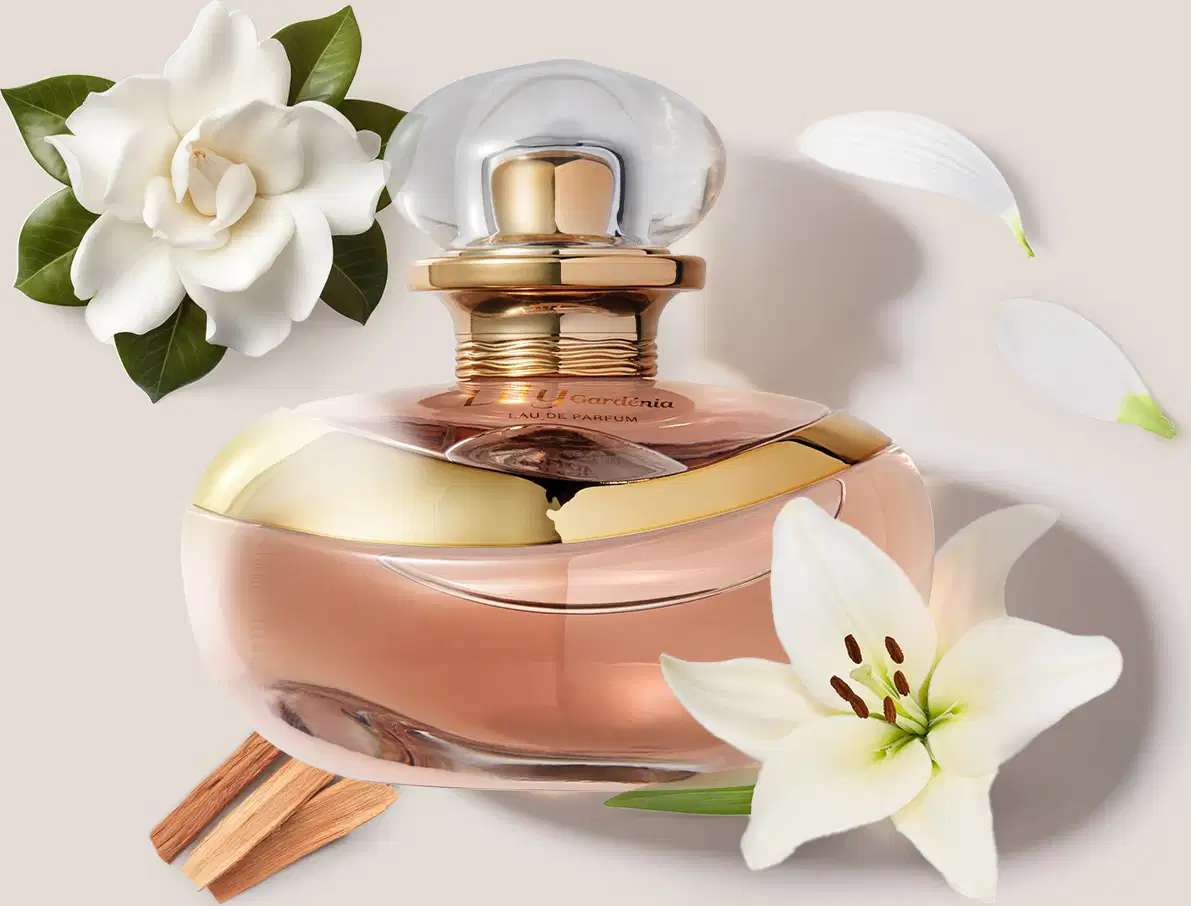 O frasco de Eau de Parfum Lily Gardênia tem formato arredondado com tampa esférica. Ao redor, há uma flor gardênia branca, pétalas de lírio branco e gravetos de canela. O conjunto transmite uma atmosfera floral