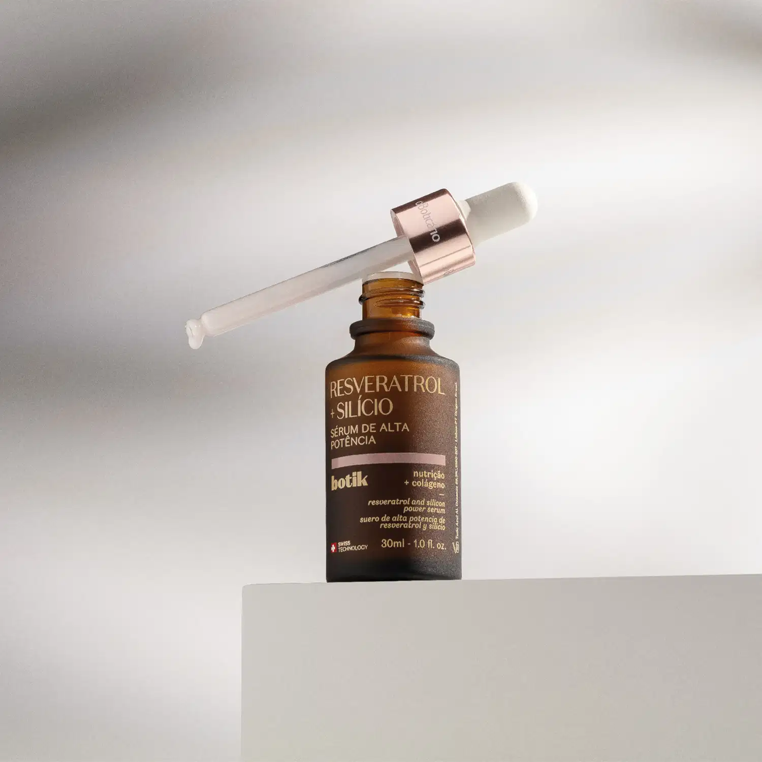 Frasco marrom com tampa dourada, conta-gotas branco e letras amarelas cde sérum de alta potência Botik Resveratrol e Silício em cima de uma plataforma branca em fundo claro com sombras.