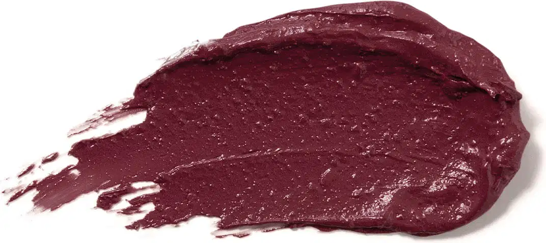 Textura cremosa e brilhante do batom glossy na cor Vinho Blackbarry da marca Make B. A aparência é brilhante e leve e está espalhada em superfície branca.