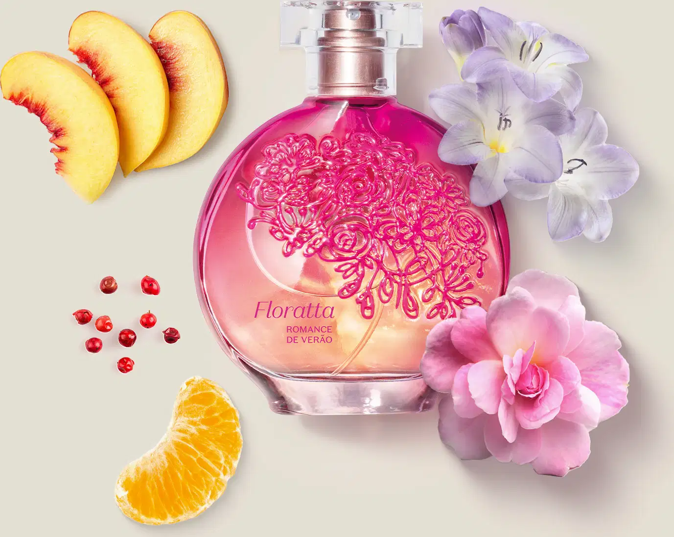 Vidro redondo com líquido rosa, floral em relevo rosa escuro, pulverizador prateado e tampa transparente contendo desodorante colônia Floratta Romance de Verão com flores e fatias de frutas cítricas em superfície clara.