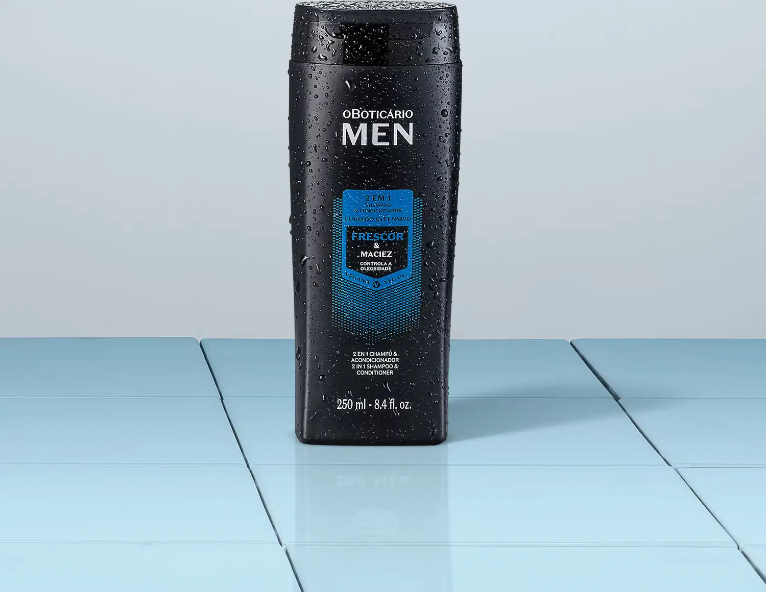 Frasco preto com detalhes azuis e letras brancas contendo 250ml de shampoo e condicionador 2 em 1 da marca Men em fundo cinza e superfície da mesma cor simulando tábuas.