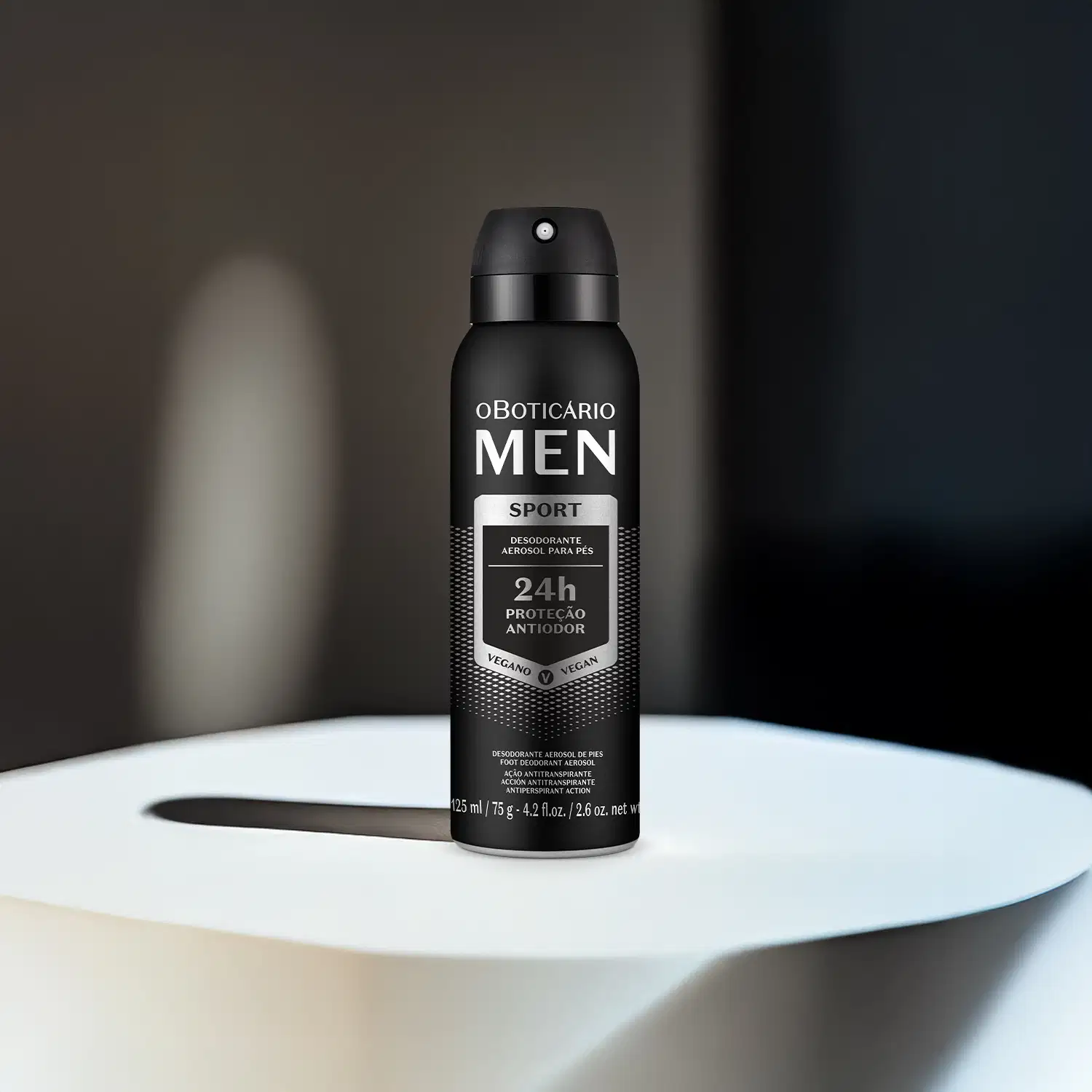 Frasco preto com detalhes prateados e letras brancas de desodorante aerossol para os pés da marca Men Sport em superfície iluminada e fundo escuro.