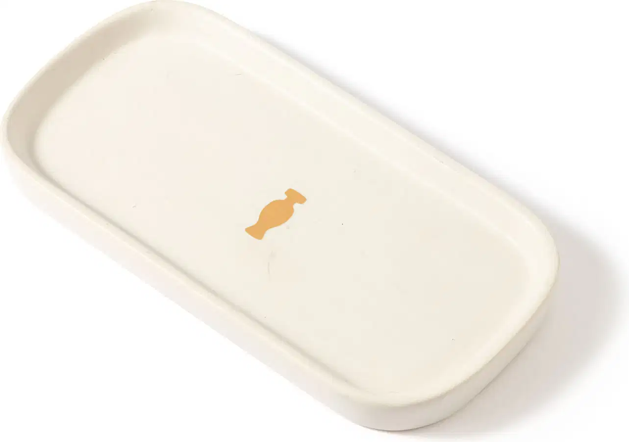 Bandeja para lavabo branca da marca Casa 214 no formato retangular com cantos arredondados e com logo do Boticário em dourado no centro.