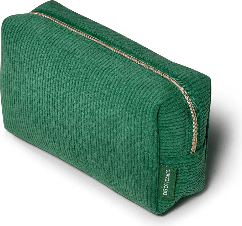 O produto apresentado é uma necessaire de cor verde, com um design de linhas retas e textura canelada com zíper dourado que percorre toda a extensão da peça, permitindo acesso ao seu interior. O logo da marca "O Boticário" é visível na parte frontal