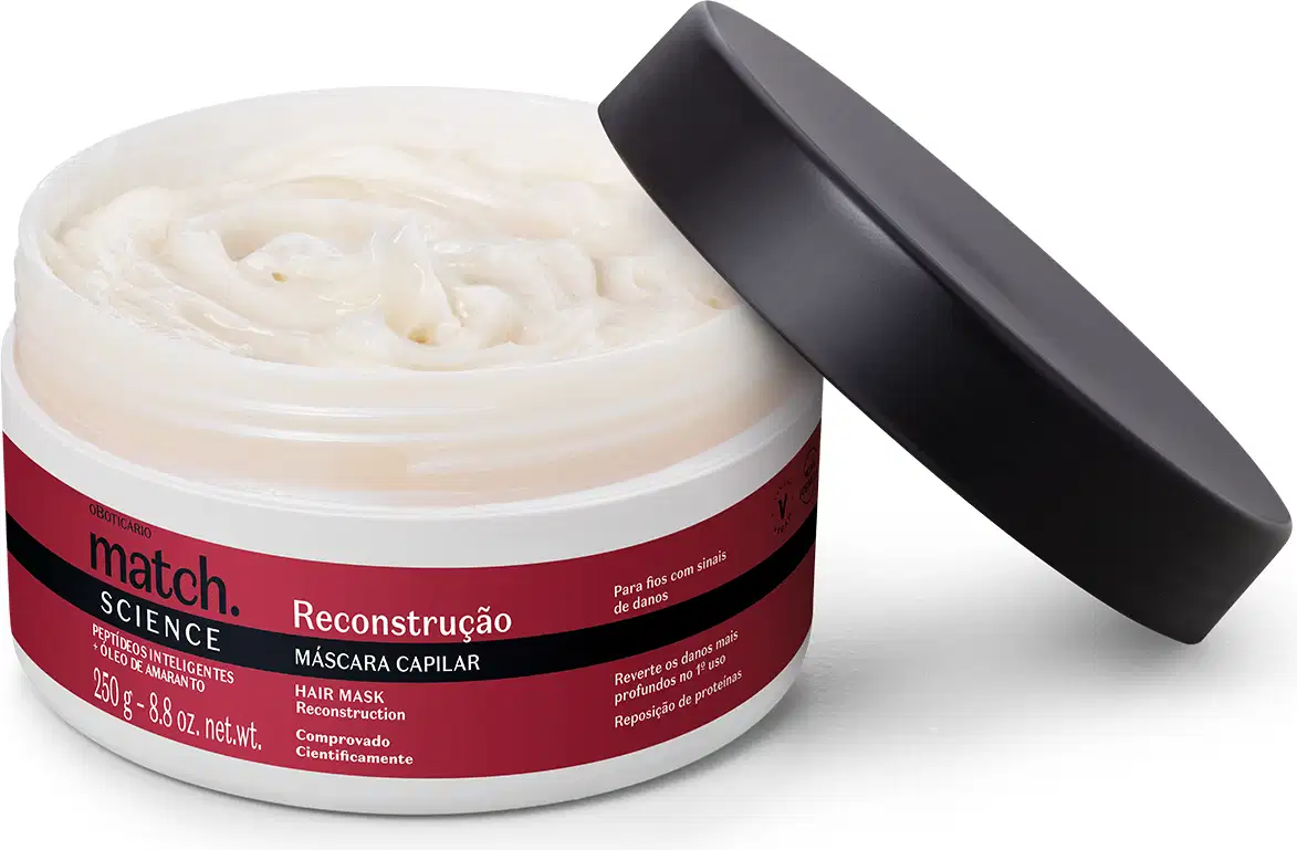 Pote branco aberto com creme branco dentro dele e tampa preta apoiada na embalagem. O produto possui rótulo na cor vermelha metalizada, preto e branco.