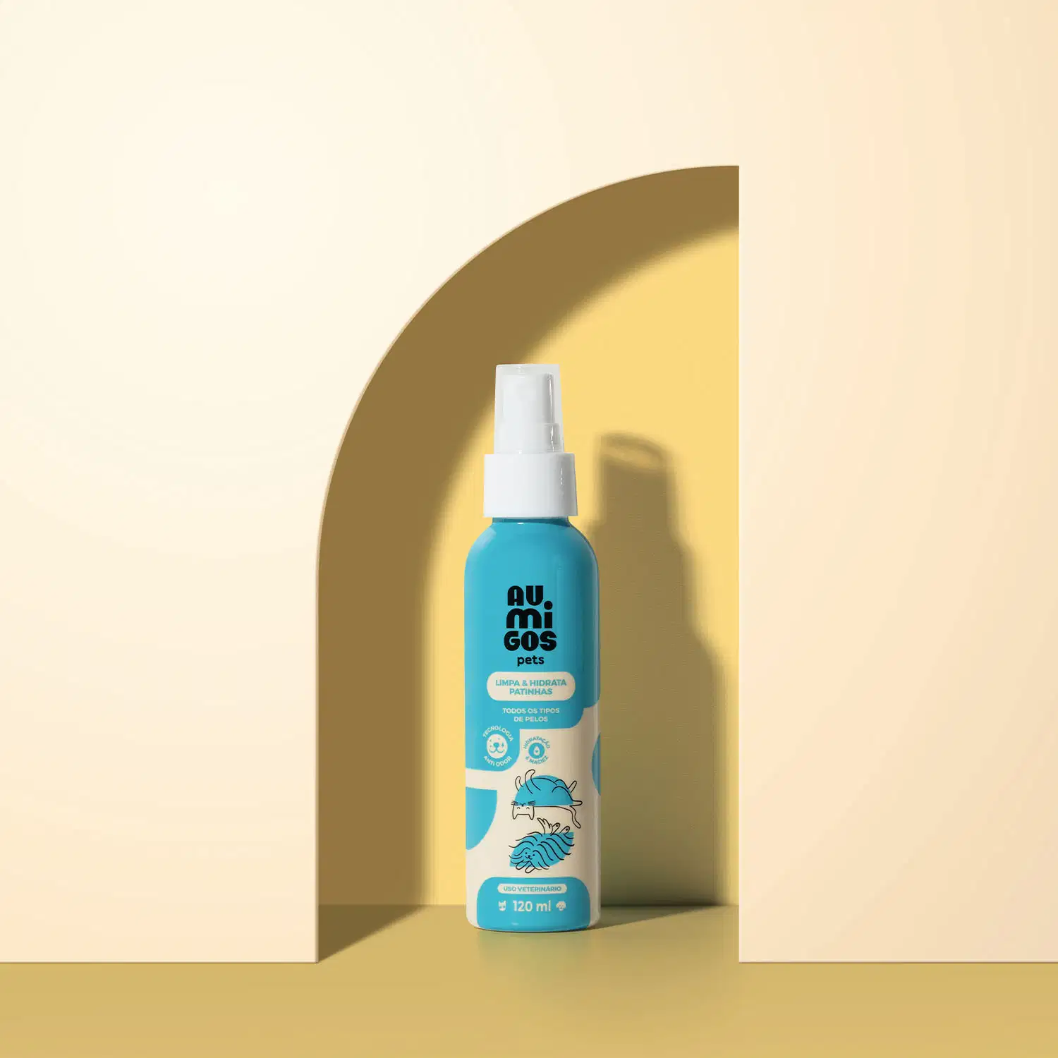 Frasco em tons de azul e rosa com tampa spray branca e letras pretas contendo 120ml de limpa e hidrata patinhas da marca Au.Migos. O produto está dentro de um arco com fundo e superfície em tons de laranja.