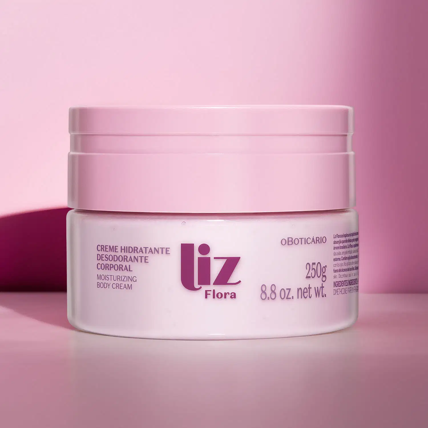 Pote rosa claro com tampa rosa e letras vinho contendo 250g de creme hidratante corporal Liz Flora em fundo rosa com sombras.