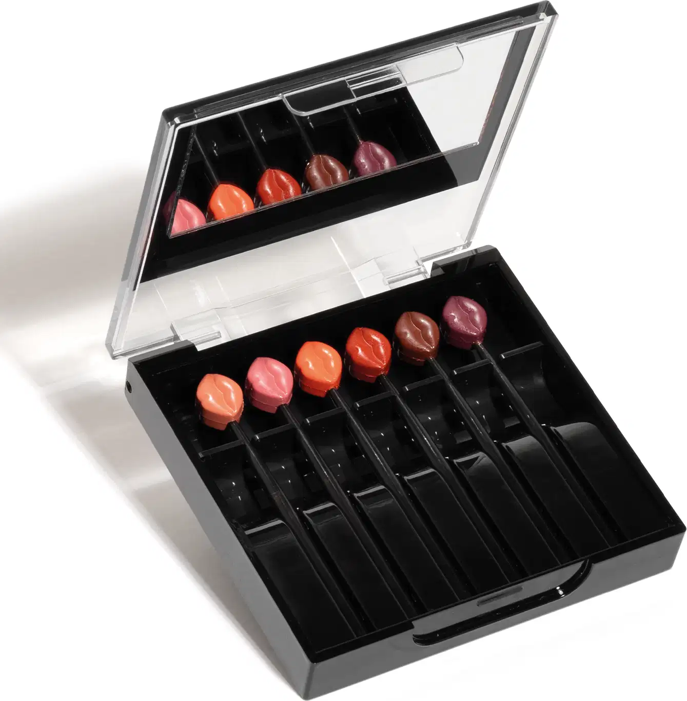 Estojo preto com seis mini batons de diferentes tonalidades de rosa e vermelho com espelho na tampa da marca Make B. Six Mini Lips.