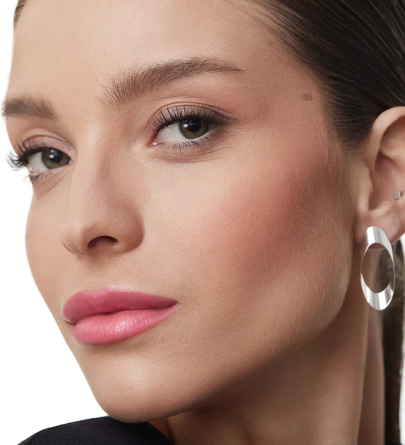 A imagem mostra um close-up do rosto de uma mulher usando maquiagem. Ela tem sobrancelhas bem delineadas em um tom castanho escuro. Seus olhos estão realçados com sombra marrom delineador e cílios volumosos. Os lábios estão com um batom rosado brilhante.