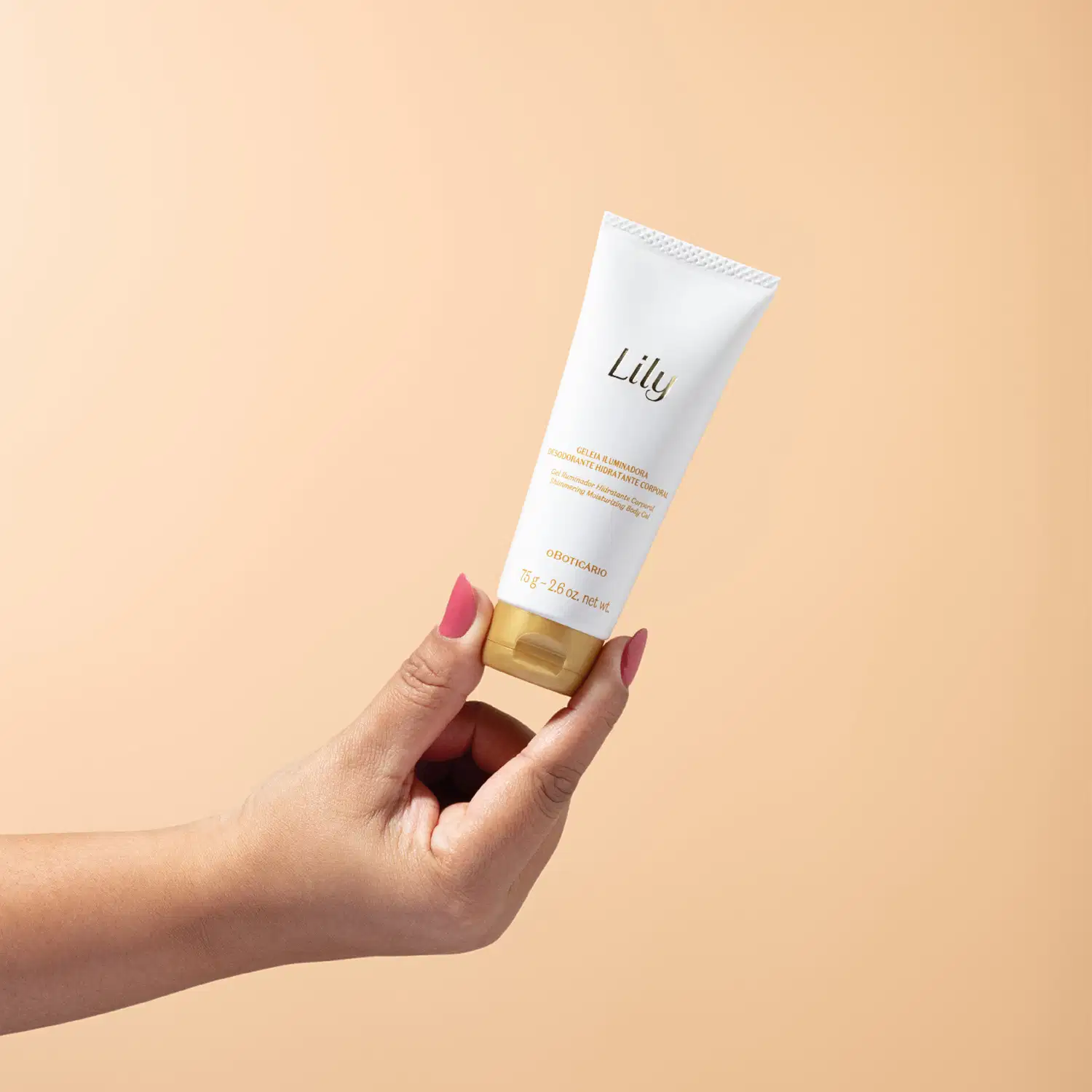 Mão feminina segurando um frasco branco com letras e tampa em dourado contendo 75g de geleia iluminadora hidratante corporal da marca Lily em fundo em tons de rosa.