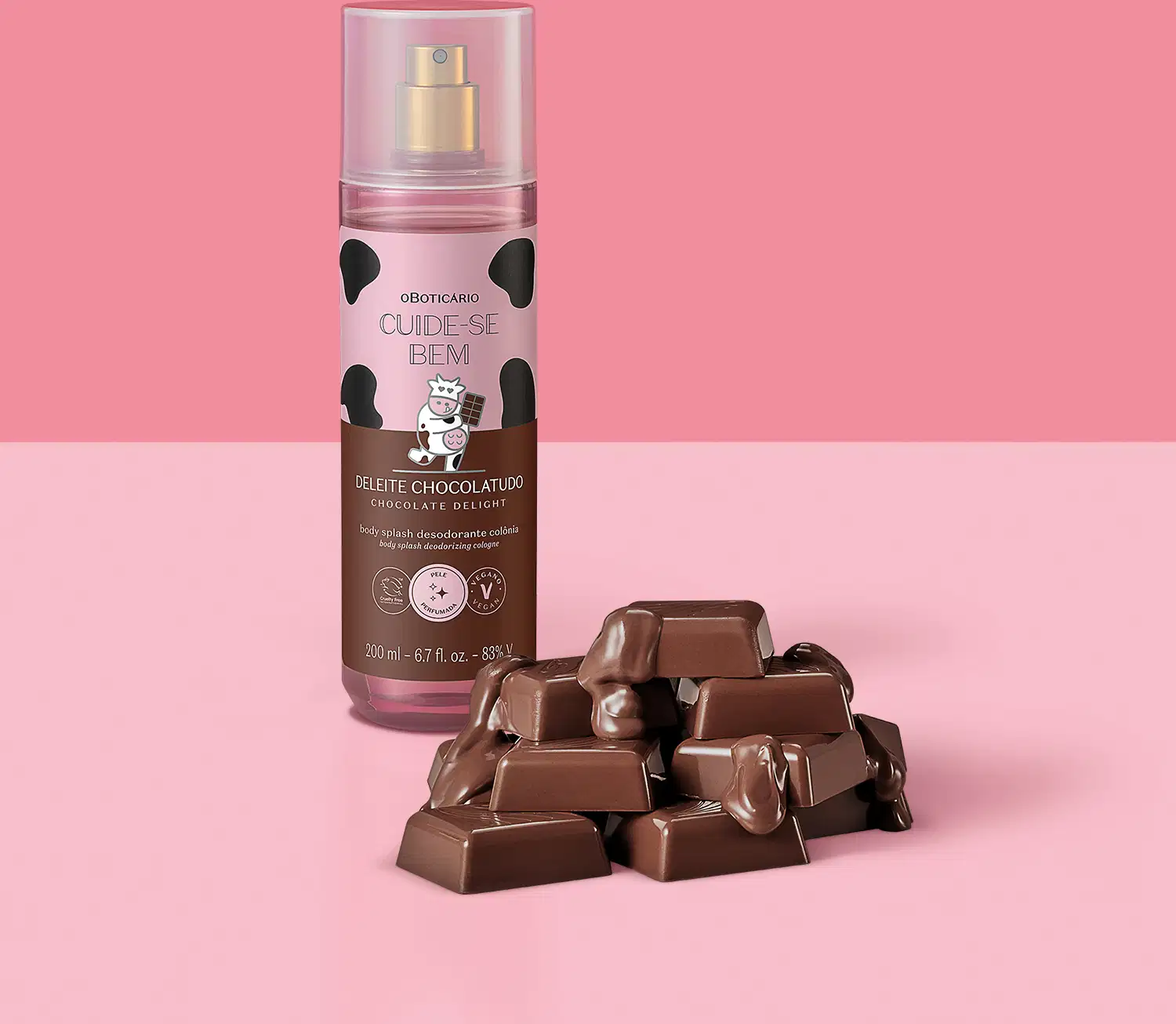 Frasco com rotulo rosa e marrom com vaca ilustrada de body splash Cuide-se Bem Deleite Chocolatudo com pedaços de chocolate ao leite espalhados ao lado do frasco, representando o aroma do produto em fundo rosa.