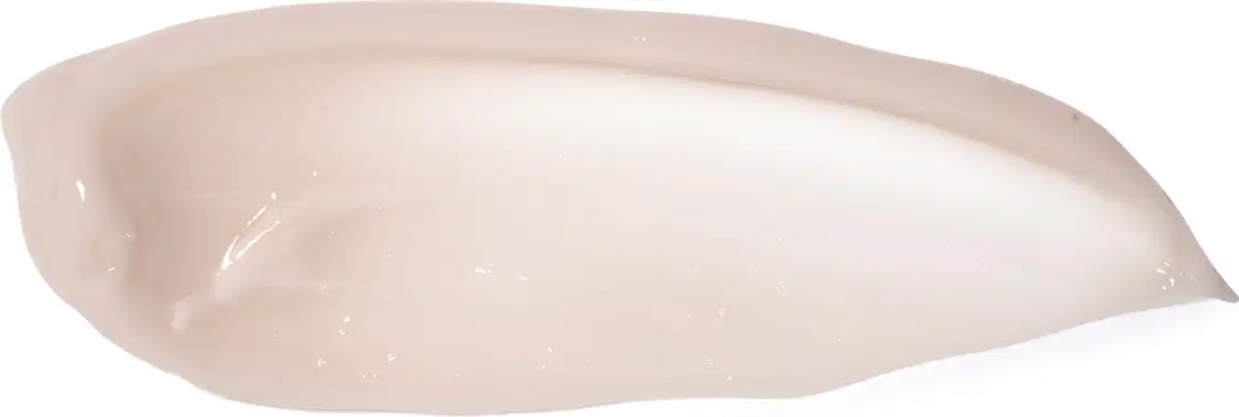 Produto de beleza em forma de creme corporal. Apresenta uma textura cremosa e brilhante na cor bege claro. O produto está disposto em uma forma alongada e curva, semelhante a uma concha ou espiral. Não há embalagem ou rótulos visíveis.