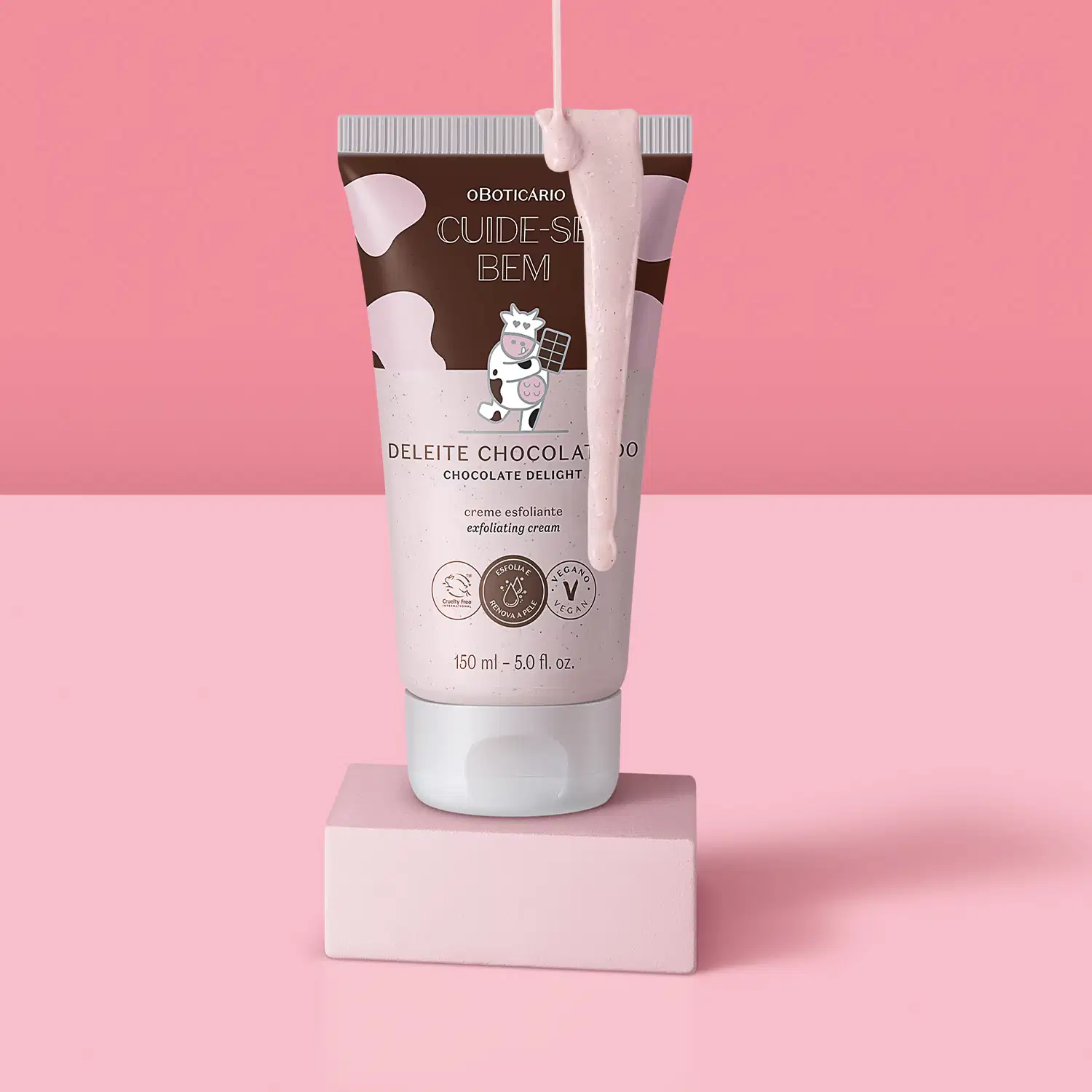 Frasco rosa e marrom com ilustração de uma vaquinha contendo creme esfoliante corporal Cuide-se Bem Deleite em uma plataforma branca com creme escorrendo sobre a embalagem, em fundo e superfície em tons de rosa.