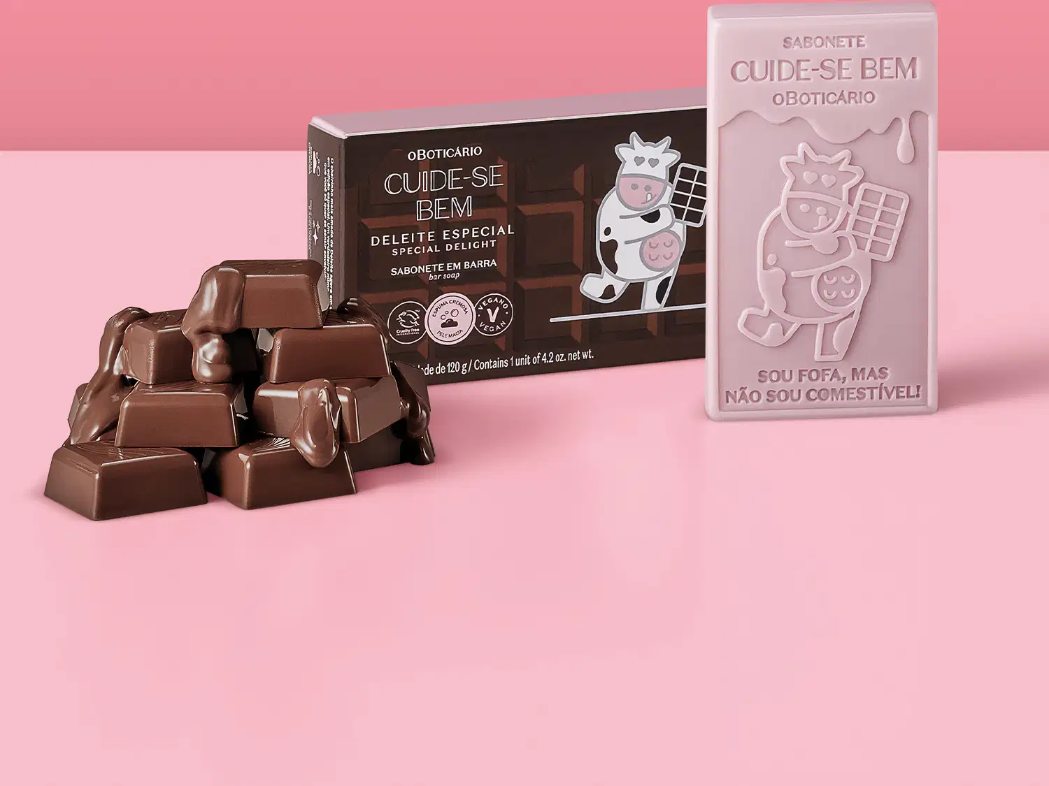 Sabonete em barra de chocolate com embalagem especial. Embalagem marrom com ilustração de uma vaca usando um avental e segurando uma barra de chocolate. Sabonete com ilustração de uma vaca e texto "Sou fofa, mas não sou comestível!".