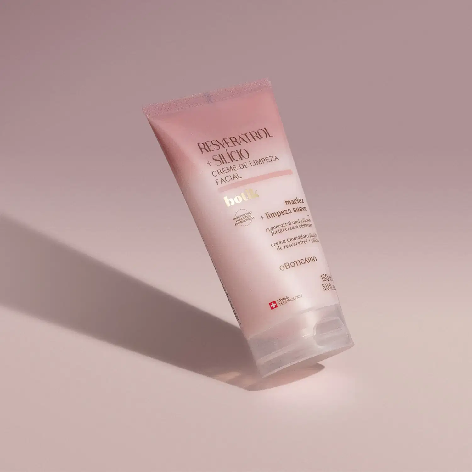 Bisnaga com degradê de rosa e branco e letras marrons de creme de limpeza facial Botik  Resveratrol e Silício. em fundo roxo com sombras.