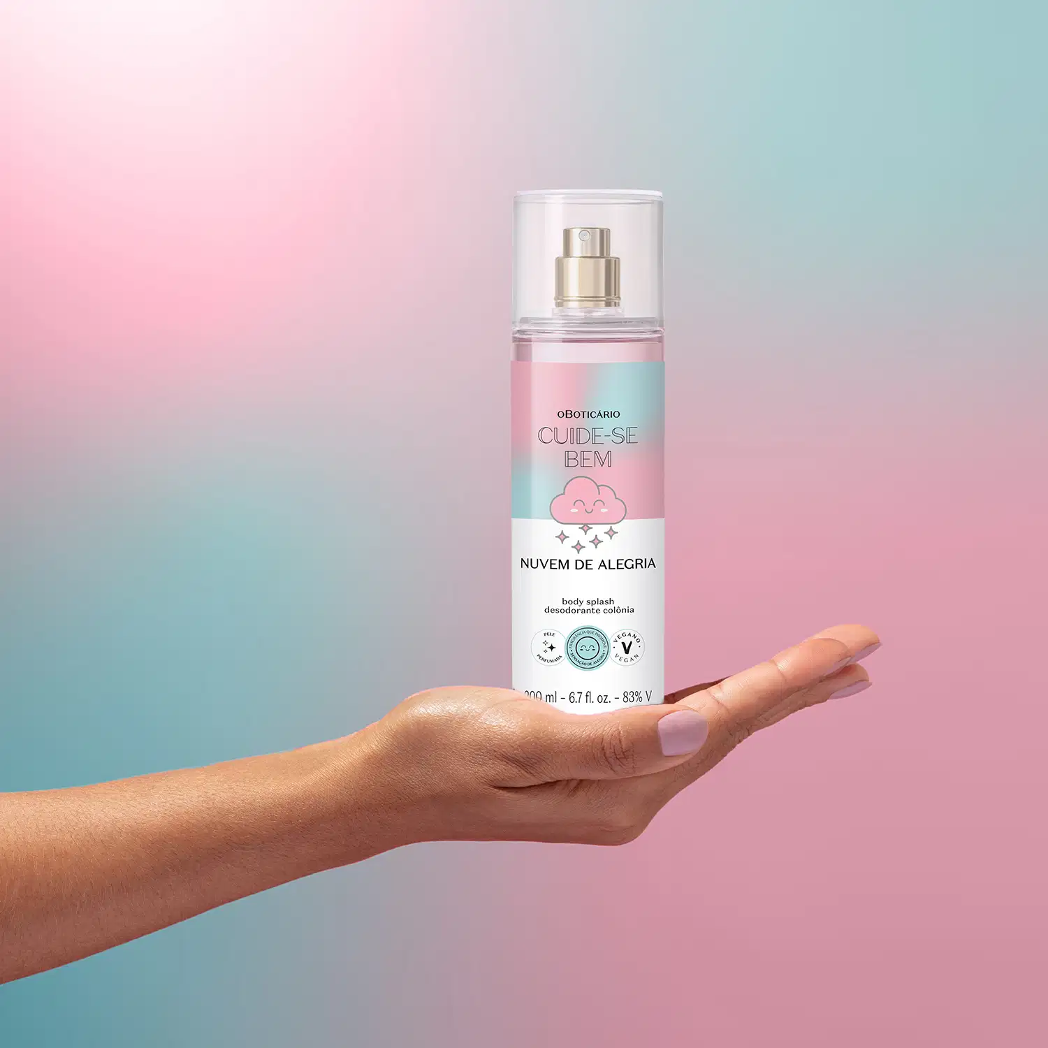 Embalagem de body splash Cuide-se Bem Nuvem de Alegria em formato de spray sobre fundo degradê rosa e azul, com nuvem estilizada sendo segurado por mão feminina.