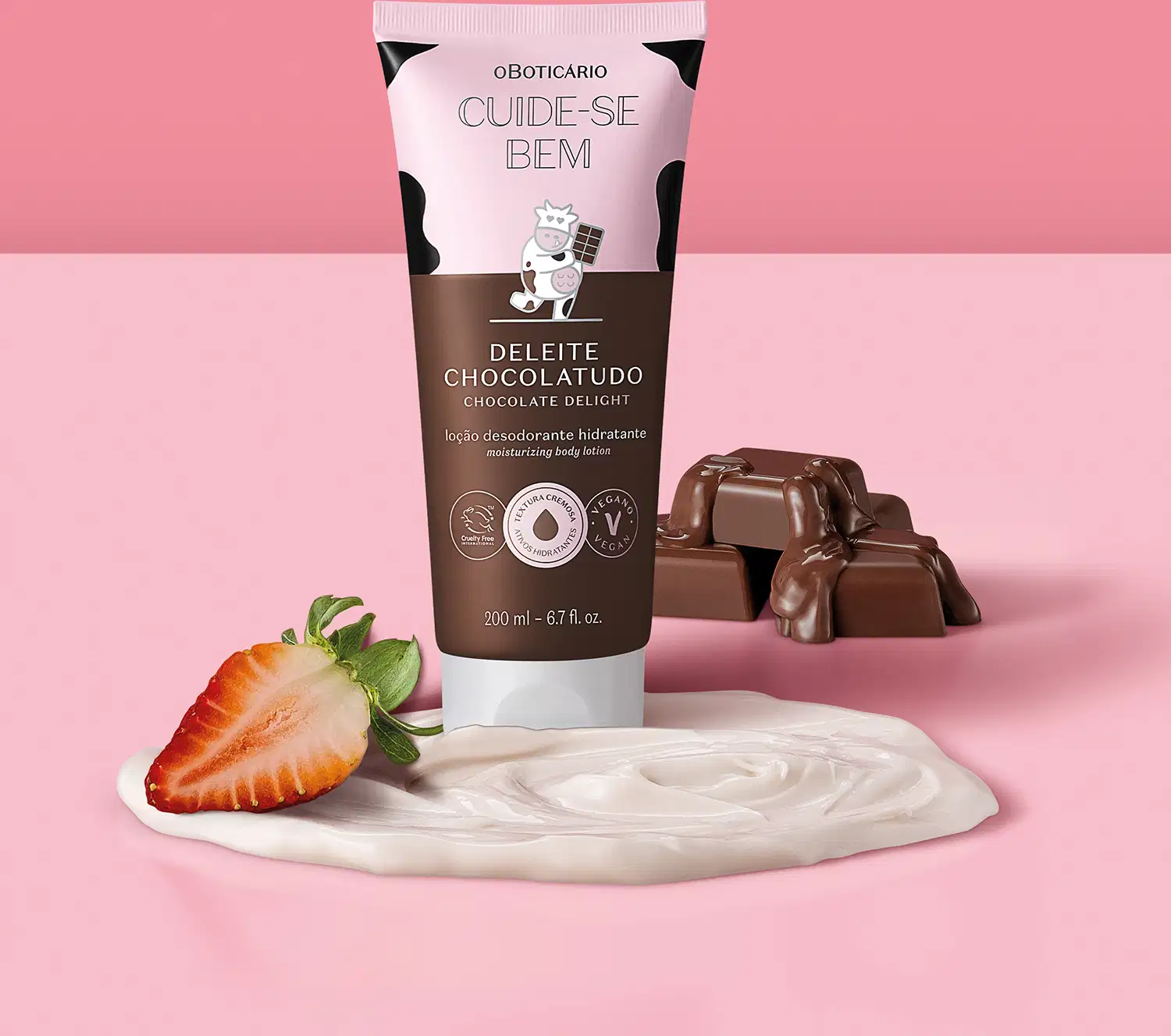 Embalagem de loção hidratante corporal Cuide-se Bem Deleite Chocolatudo ao lado de barras de chocolate, um morango cortado ao meio e um creme rosa claro, todos dispostos sobre um fundo rosa. 