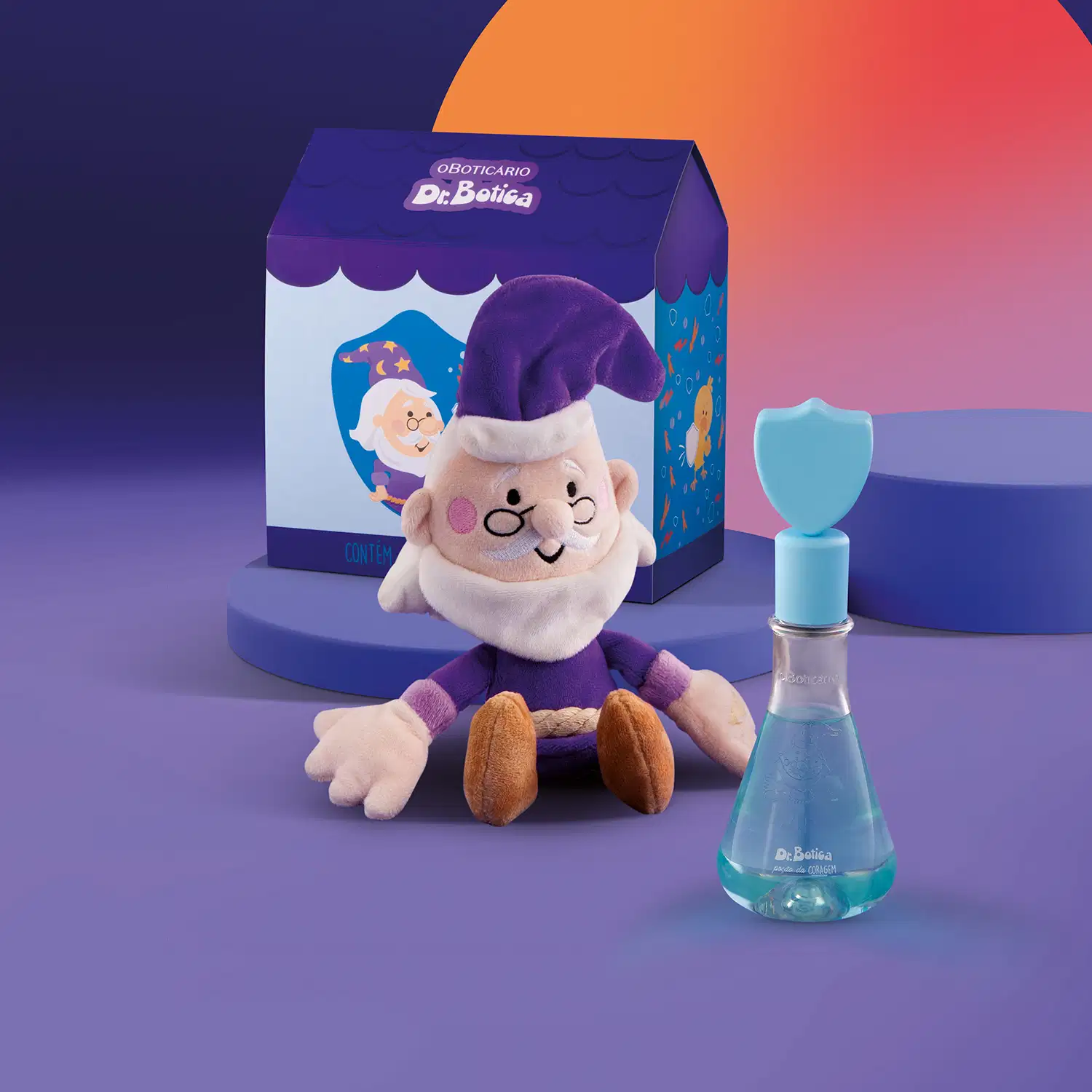 Kit Infantil Dr. Botica consiste em uma caixa azul com detalhes em branco e azul exibindo ilustrações de um personagem idoso e um urso de pelúcia. Dentro da caixa há um frasco de vidro azul contendo item de perfumaria e um brinquedo de pelúcia.