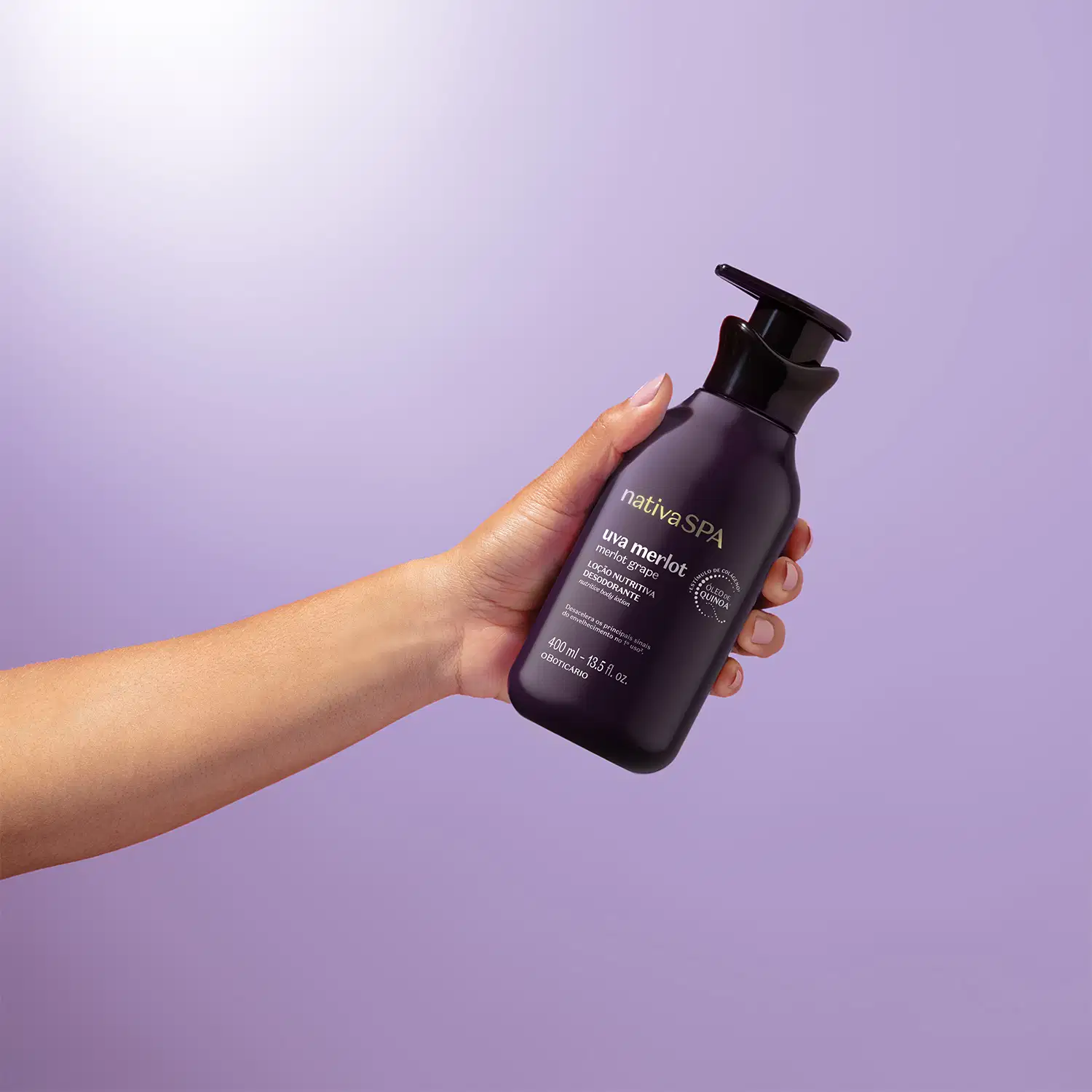 Mão feminina segurando um frasco roxo escuro e preto com letras douradas e brancas de loção hidratante corporal Nativa SPA Uva Merlot em fundo azul e branco.