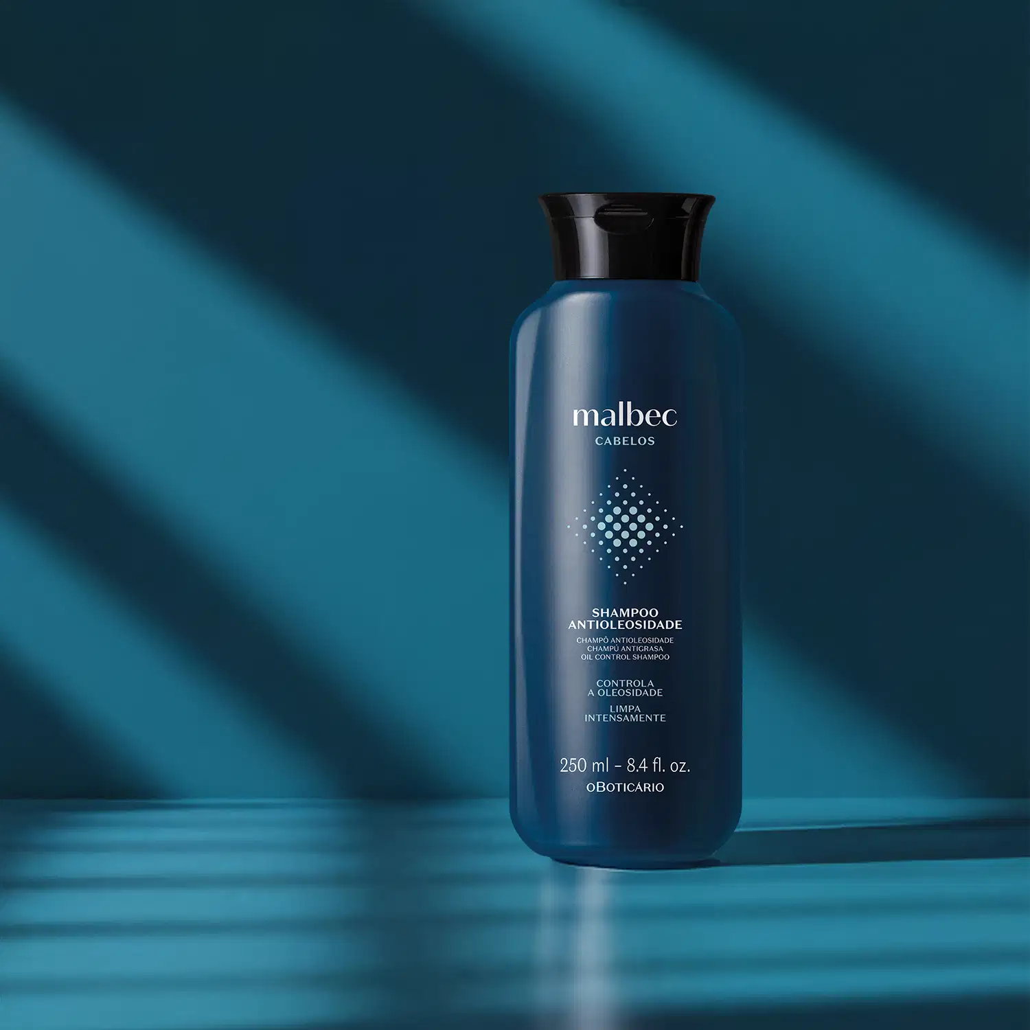 Frasco azul escuro com tampa preta, letras brancas e detalhes na cor cinza contendo 250ml de shampoo antioleosidade da marca Malbec Cabelos em fundo azul escuro com em forma de listras.