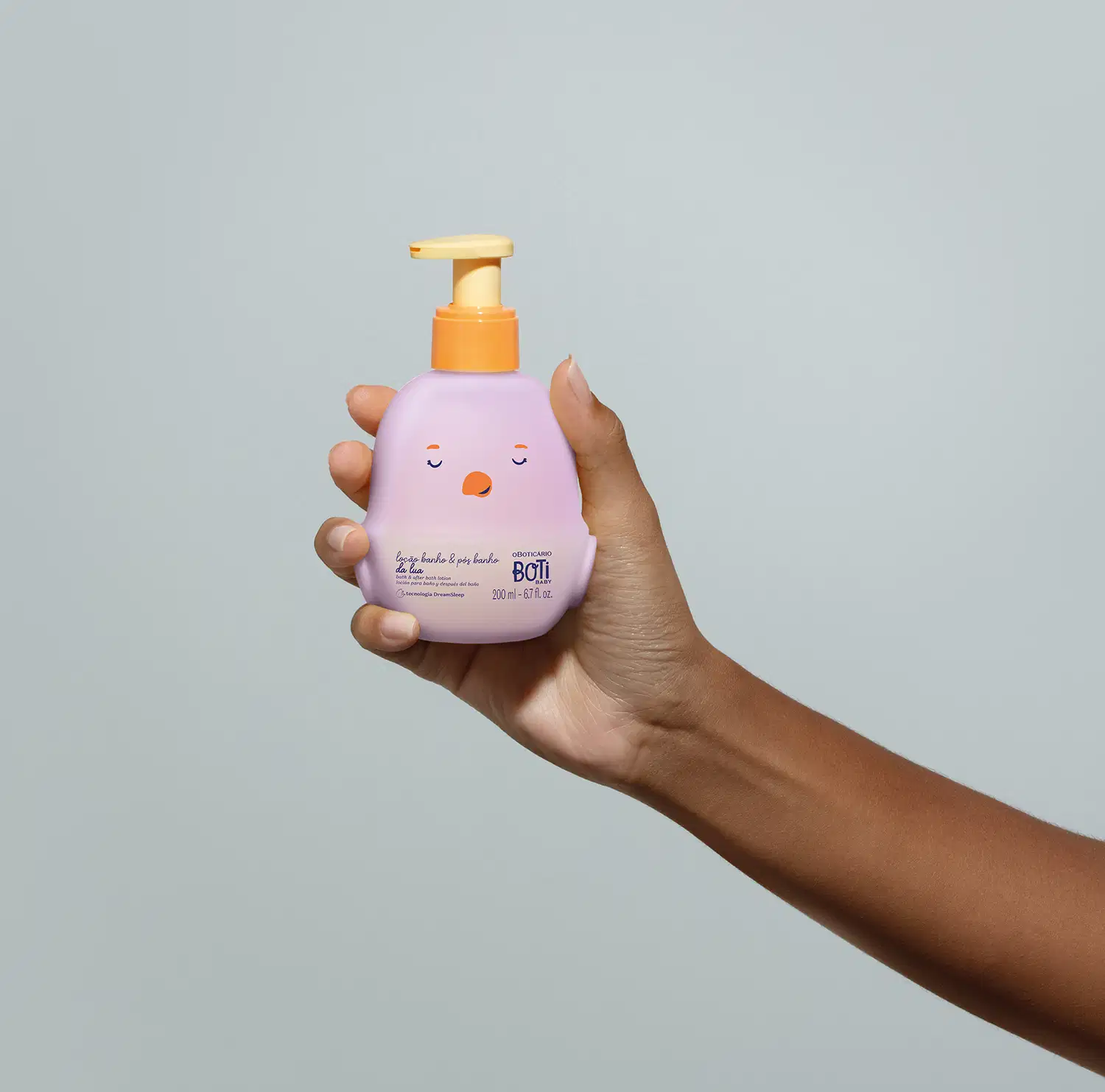 Mão feminina segurando um frasco da loção para banho e pós banho Boti Baby Lua em forma de pintinho na cor lilás e bomba dosadora laranja em fundo lilás.