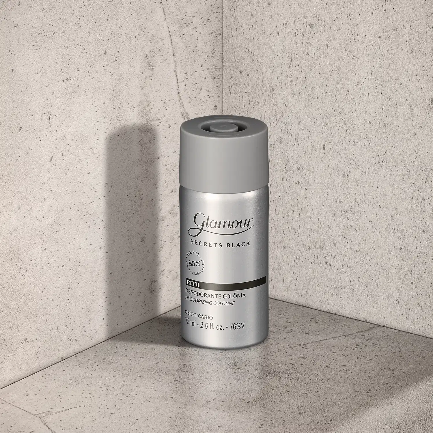Refil de desodorante colônia Glamour Secret Black em frasco prateado com tampa e letras cinzas e detalhes em preto, posicionado em canto de superfície cinza claro, com parede de concreto ao fundo e sombra projetada à esquerda.