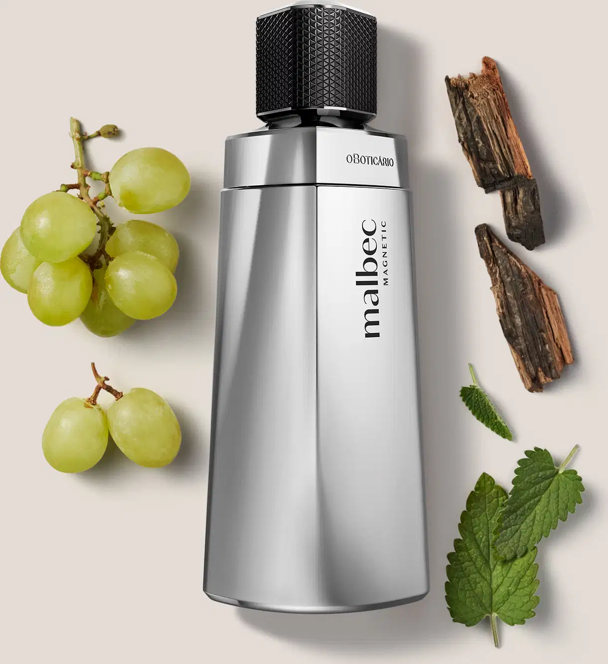 Frasco de item de perfumaria prateado com design geométrico e tampa preta. Ao redor do frasco, há alguns elementos naturais, como uvas verdes, lascas de madeira e folhas, que sugerem uma fragrância amadeirada-frutada para o produto.