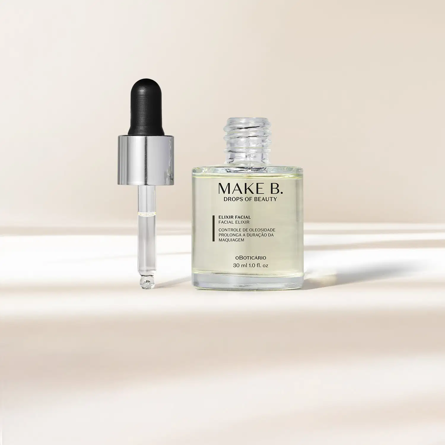 O frasco transparente com líquido claro de Elixir Facial Make B. possui tampa prateada com conta-gotas preto e está em fundo claro com sombras.