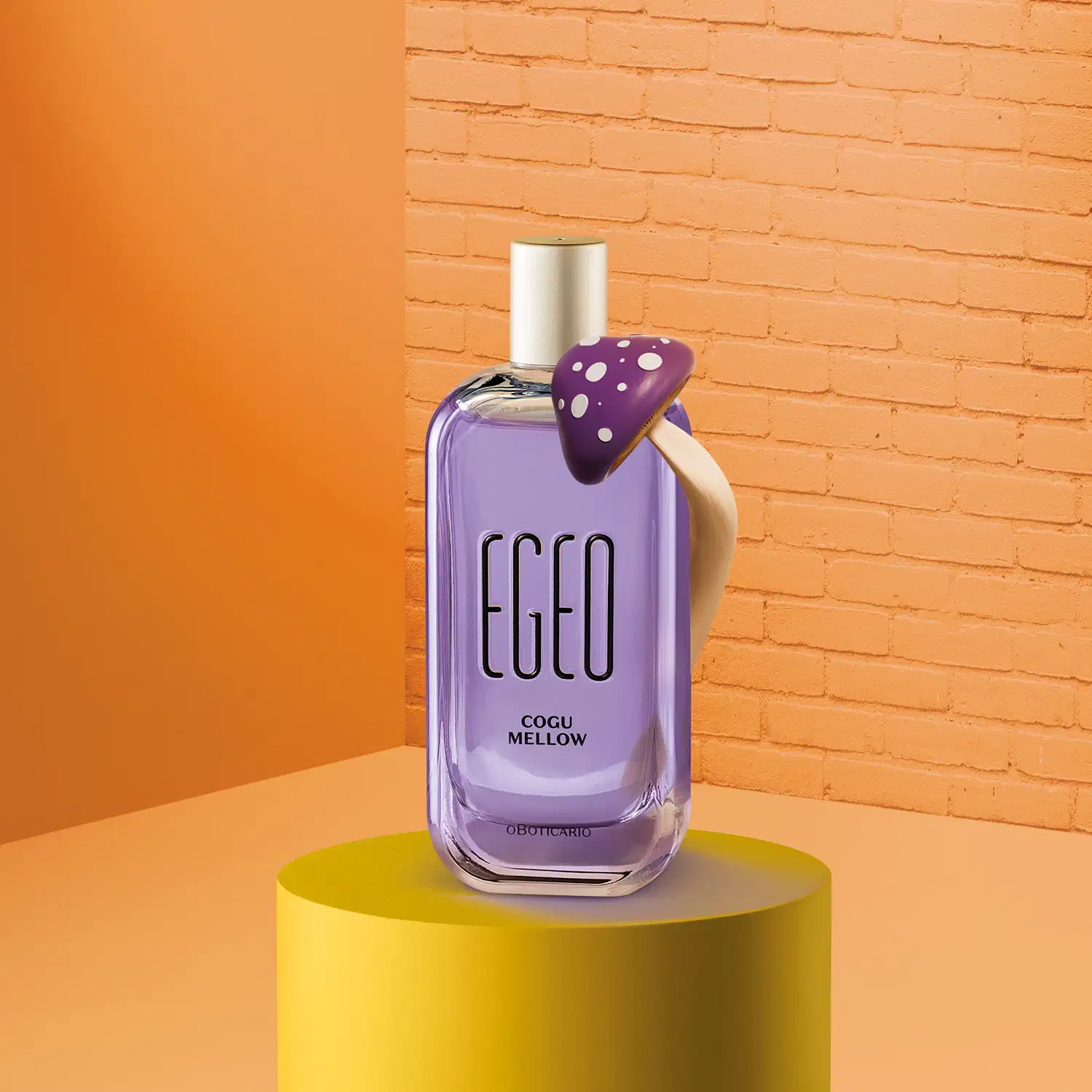 Imagem de um vidro com líquido azul e tampa prata de desodorante colônia Egeo Cogu Mellow, com cogumelo roxo e branco ao lado e fundo em tons de laranja.