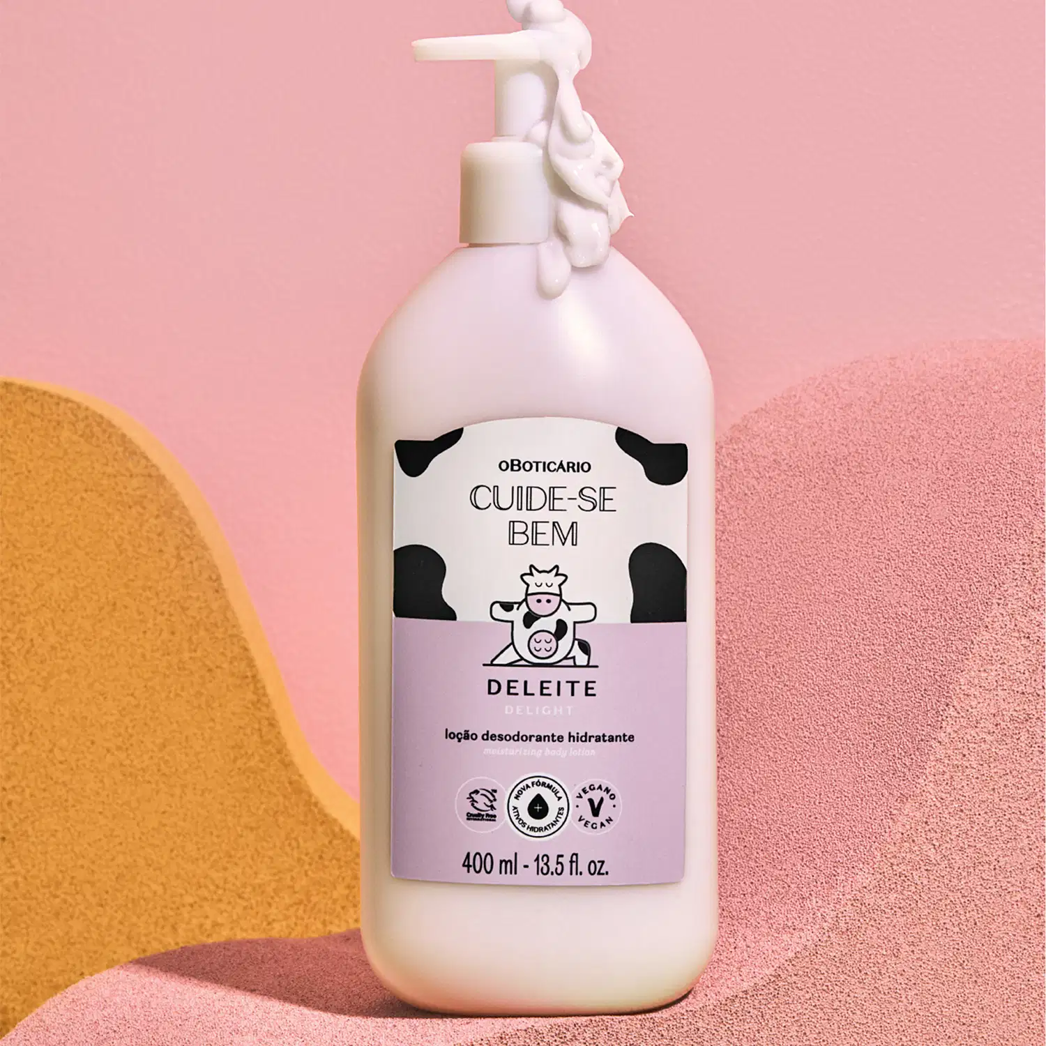 Embalagem branca com rótulo rosa e branco e ilustração de vaca de loção hidratante corporal Cuide-se Bem Deleite sobre superfície rosa e amarela com formas geométricas.