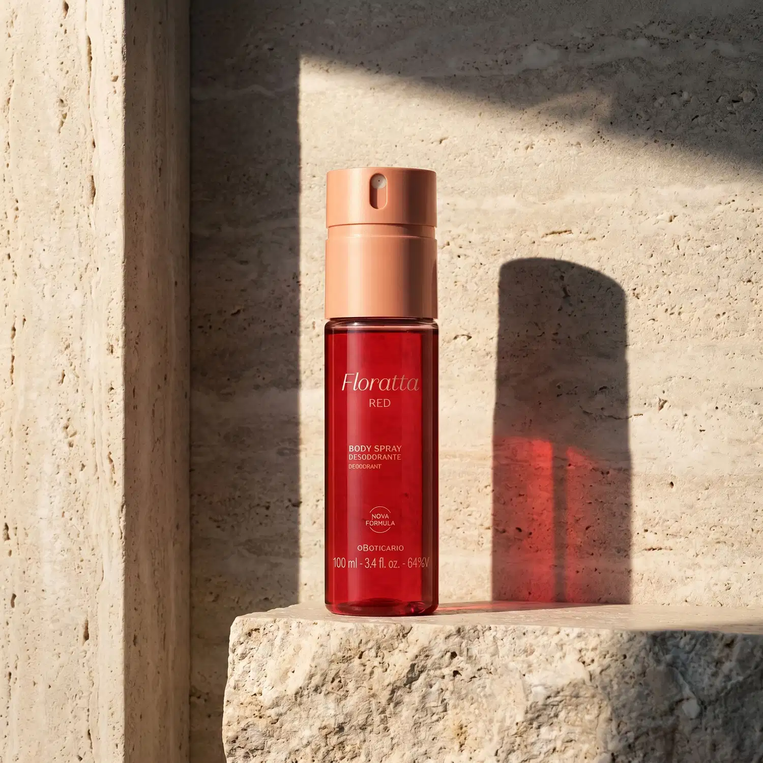 Frasco de item de perfumaria da marca Floratta Red na cor vermelha, posicionado sobre superfície de pedra clara em ambiente iluminado que forma uma sombra da embalagem no fundo de pedra da imagem.