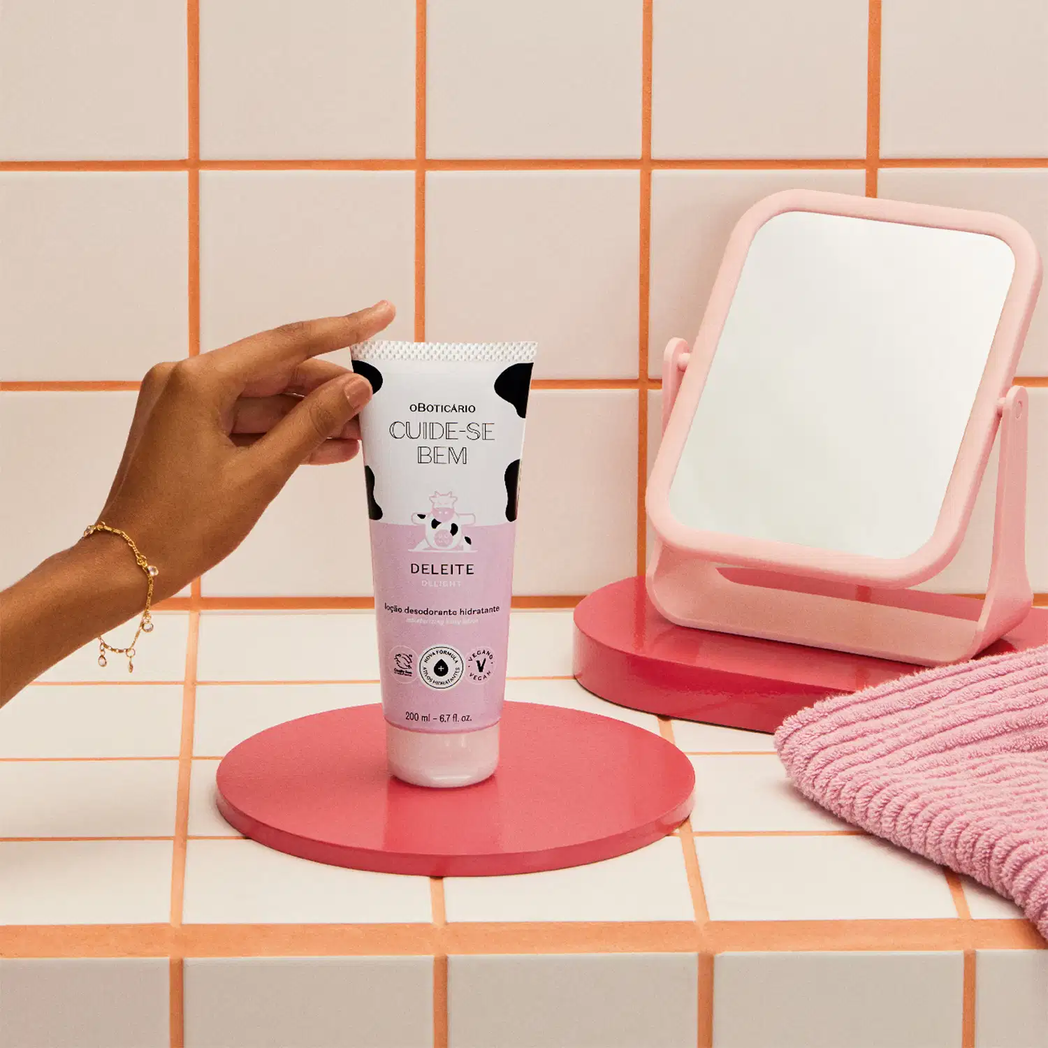 O produto exibido na imagem é um hidratante desodorante da marca Cuide-se bem, com o nome "Deleite". O frasco é branco e rosa, com um design gráfico de uma vaca. O produto está posicionado em uma superfície rosa, junto a um espelho de mesa também rosa.